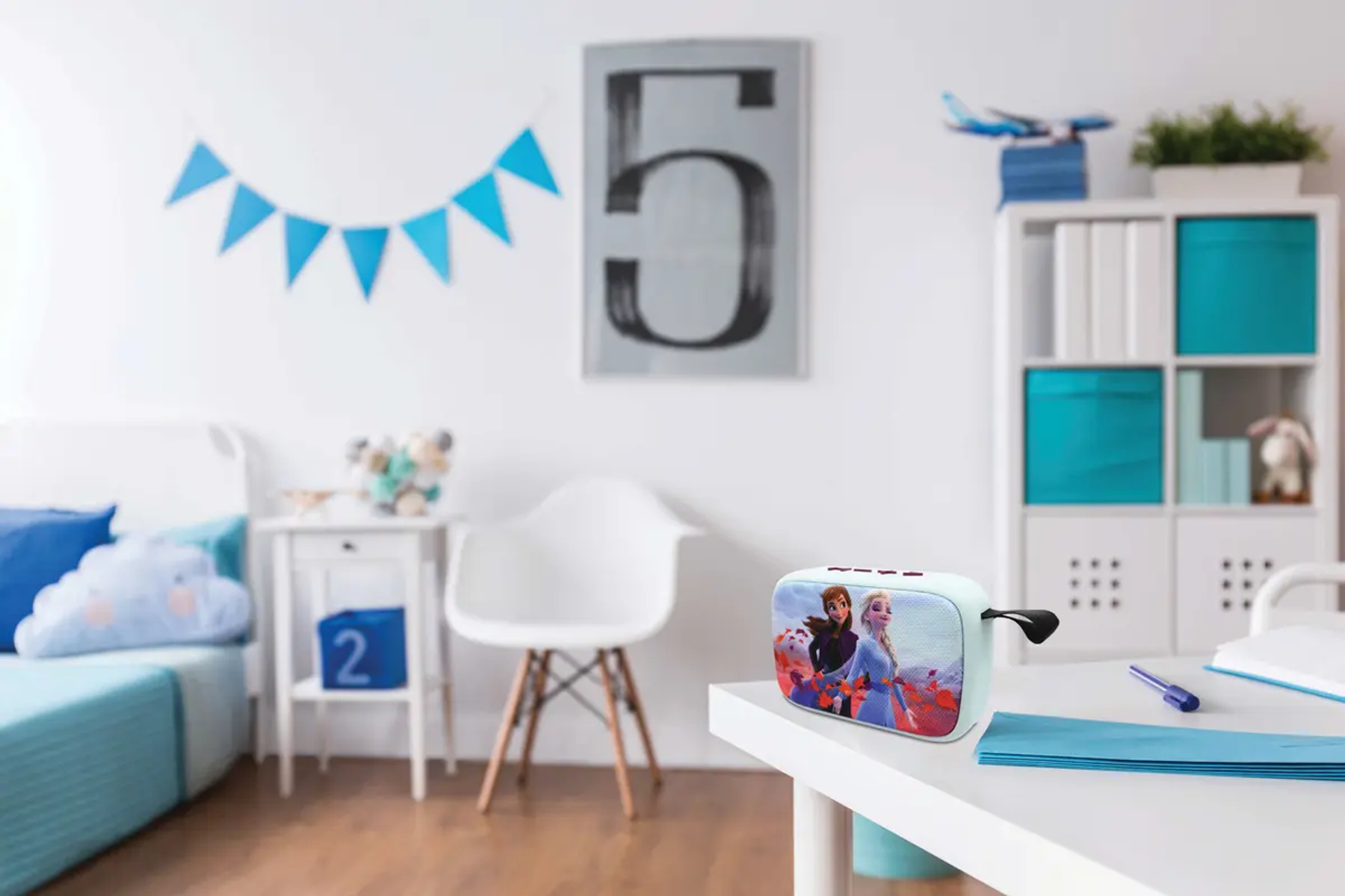 Pokój z głośnikiem z postaciami z 'Krainy Lodu'. Obecny jest biały stół, krzesło i półki. Niebieski i biały wystrój.
