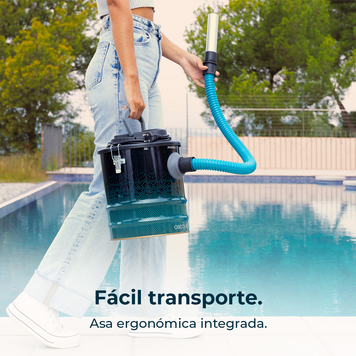Persona che tiene in mano un pulitore per piscina nero e blu. Il tubo blu si estende verso destra. Una piscina è sullo sfondo.