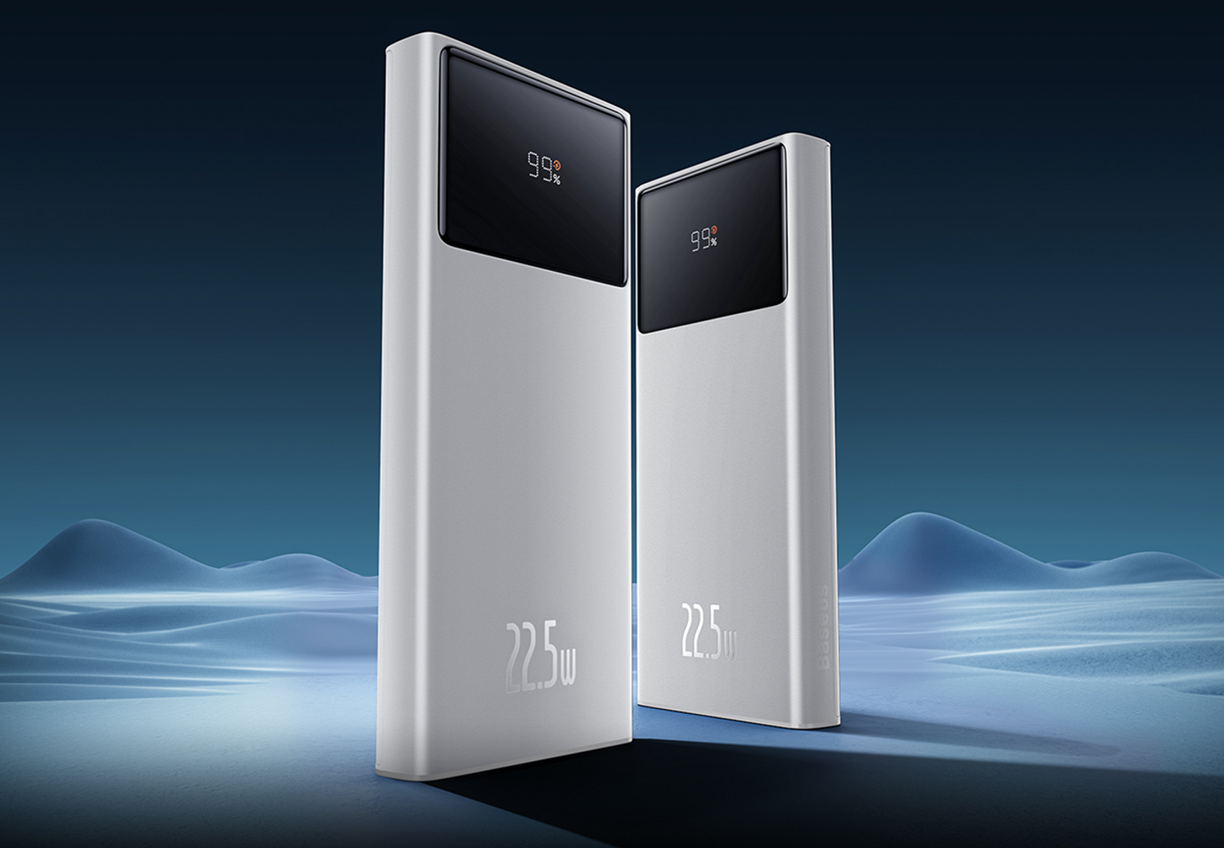 Due power bank argentati con display neri che mostrano il 99%. Hanno '22,5w' su di essi. Lo sfondo ha colline blu.