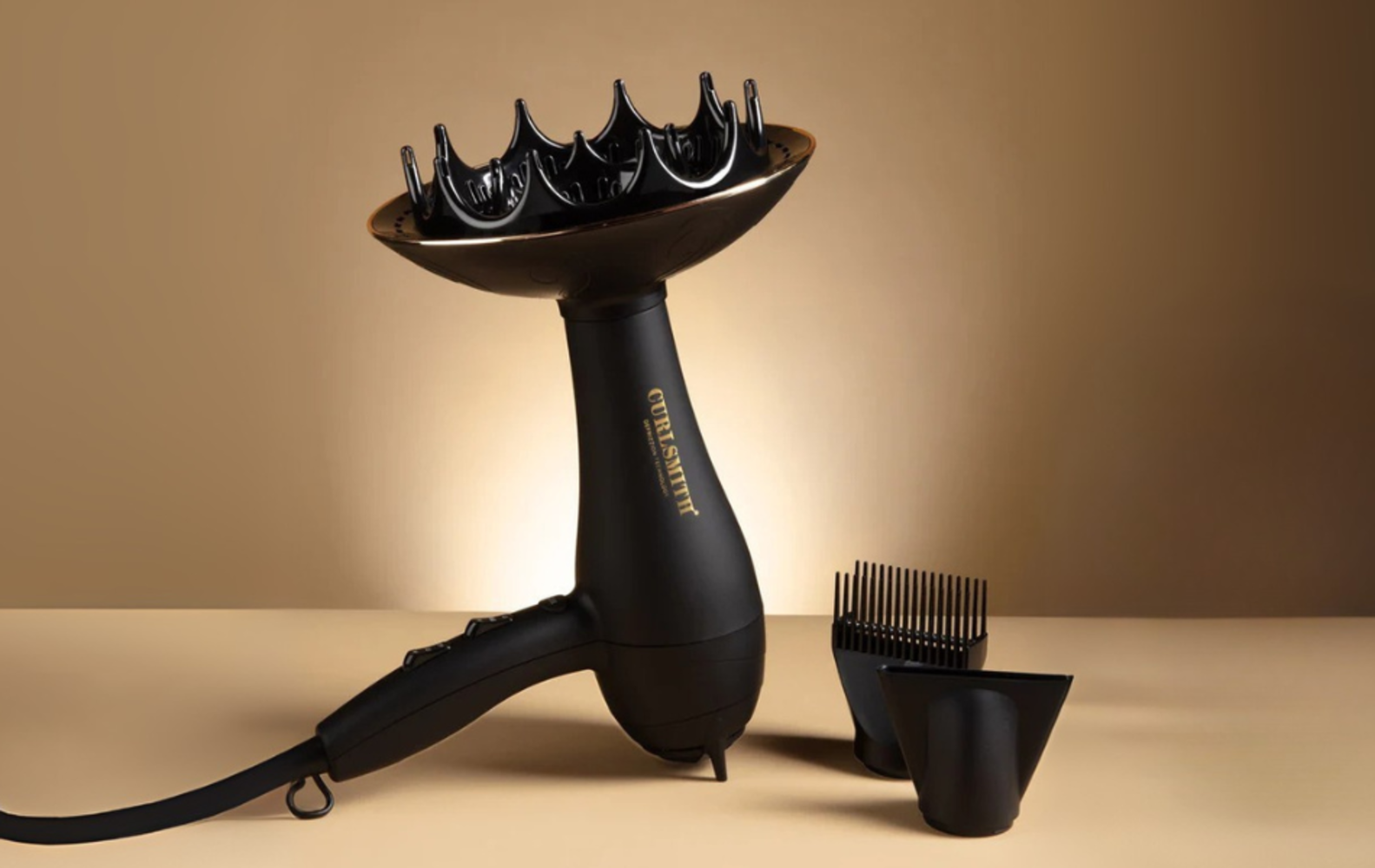 A black Curlsmith hair dryer with attachments on a beige background. A comb and concentrator nozzle are included.