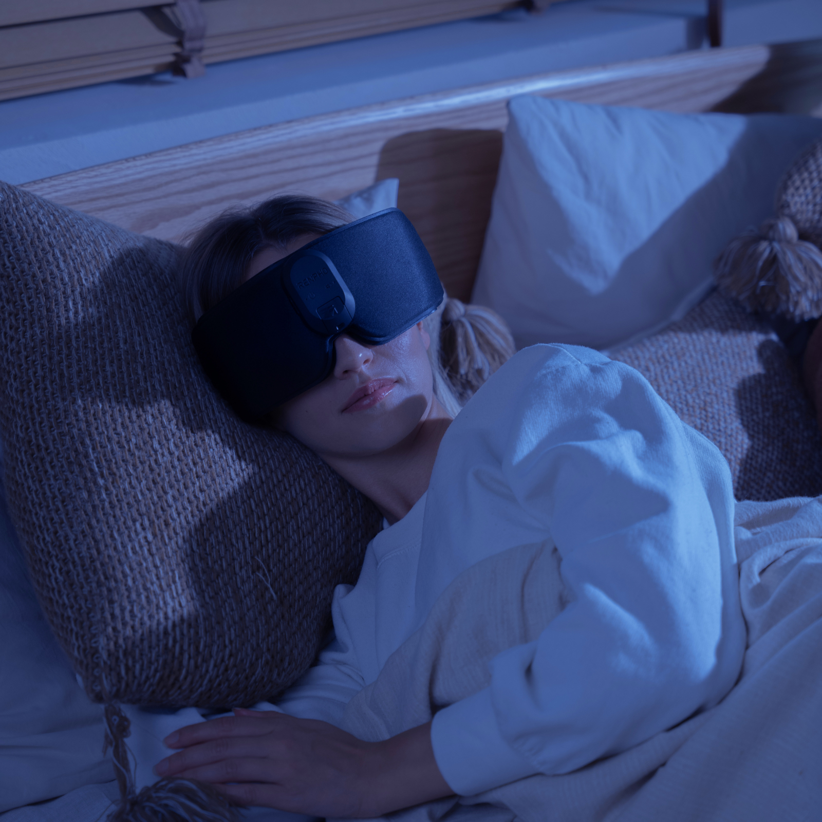 Een vrouw slaapt in bed met een slaapmasker. Ze ligt op kussens, bedekt met een deken.