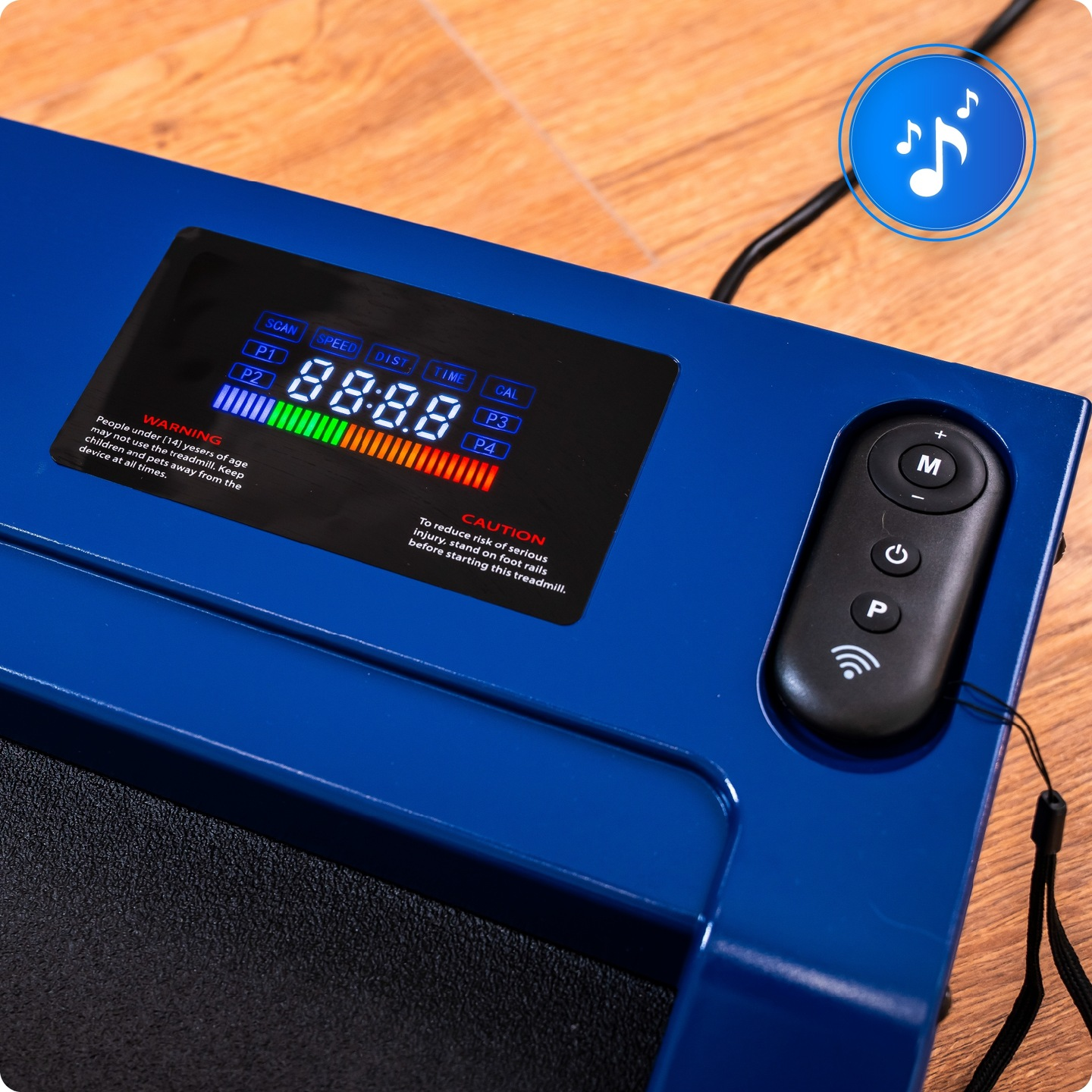 Niebieska konsola bieżni z wyświetlaczem pokazującym metryki. Widoczny jest pilot i ikona muzyki. Powierzchnia jest drewniana.