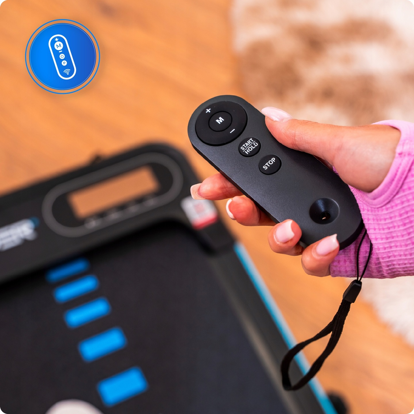 Ręka trzyma czarny pilot z przyciskami start/stop. W tle maszyna i niebieska ikona pilota.