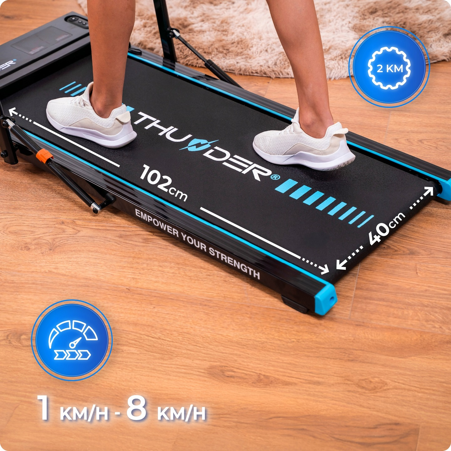 Osoba na bieżni. Bieżnia jest czarna i niebieska. Osoba ma na sobie białe trampki. Podłoga jest drewniana.