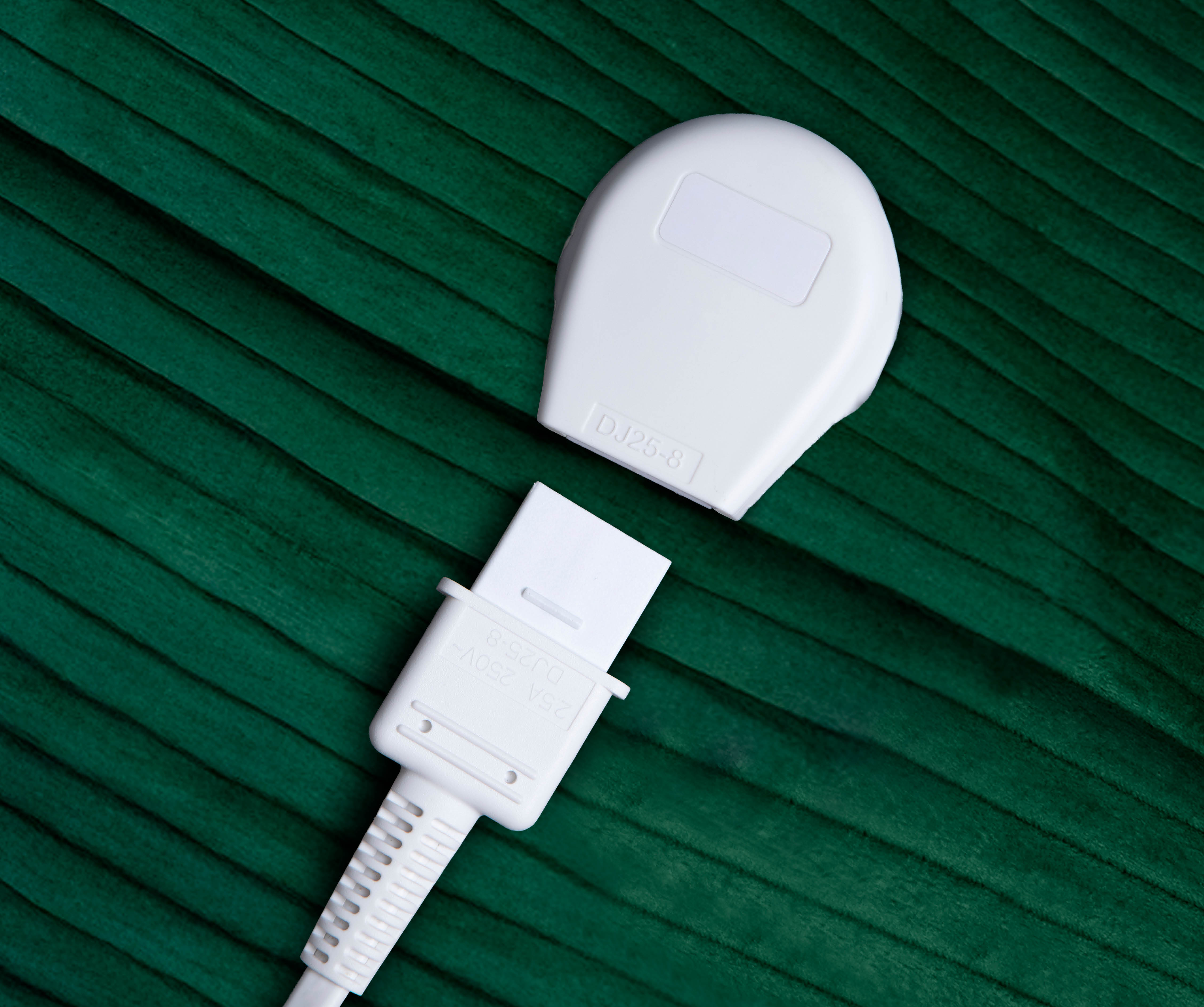 A white plug and connector, separated, against a textured, dark green background.