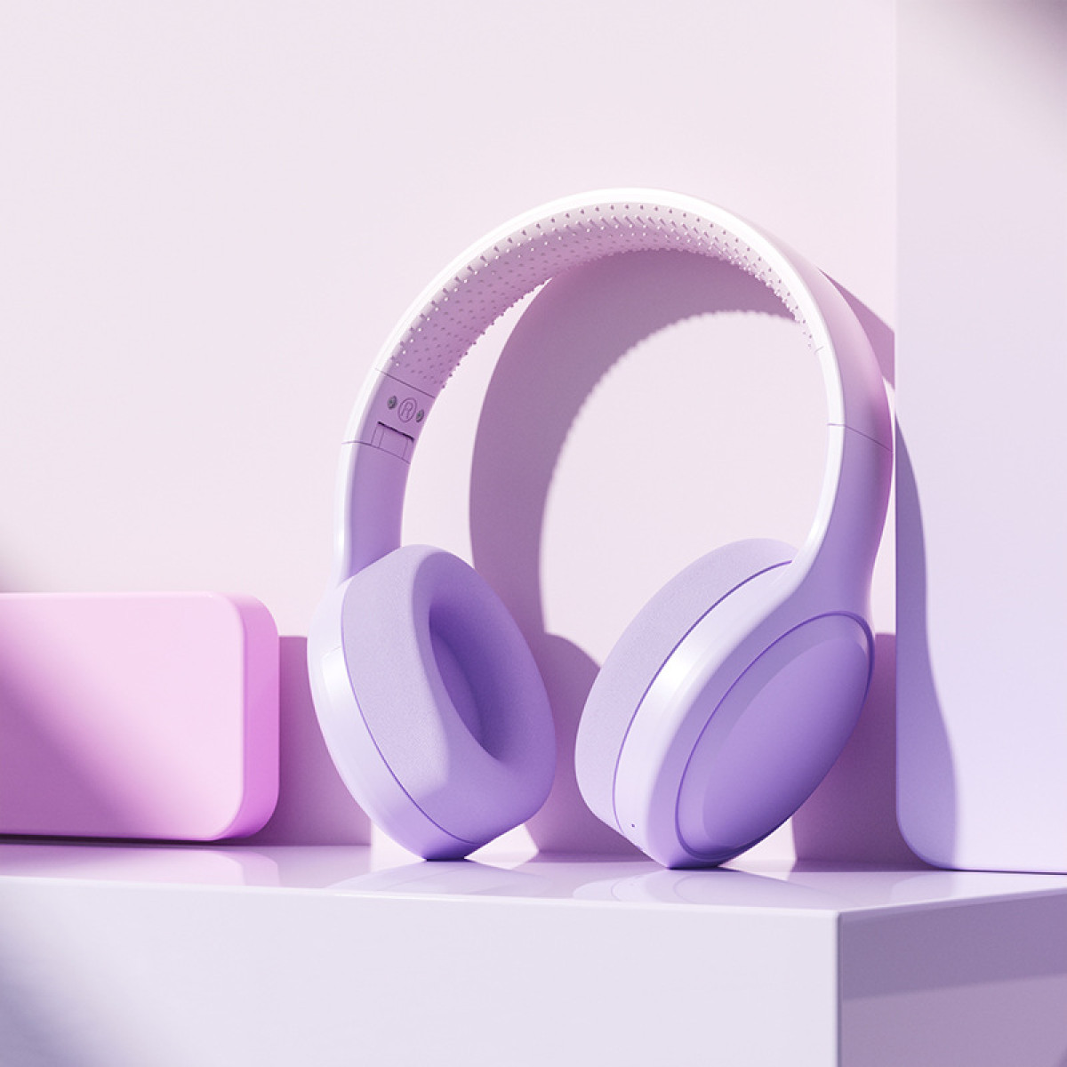 Ein Paar lavendelfarbene Kopfhörer auf einer hellvioletten Oberfläche. Ein kleines rosa Rechteck befindet sich links.