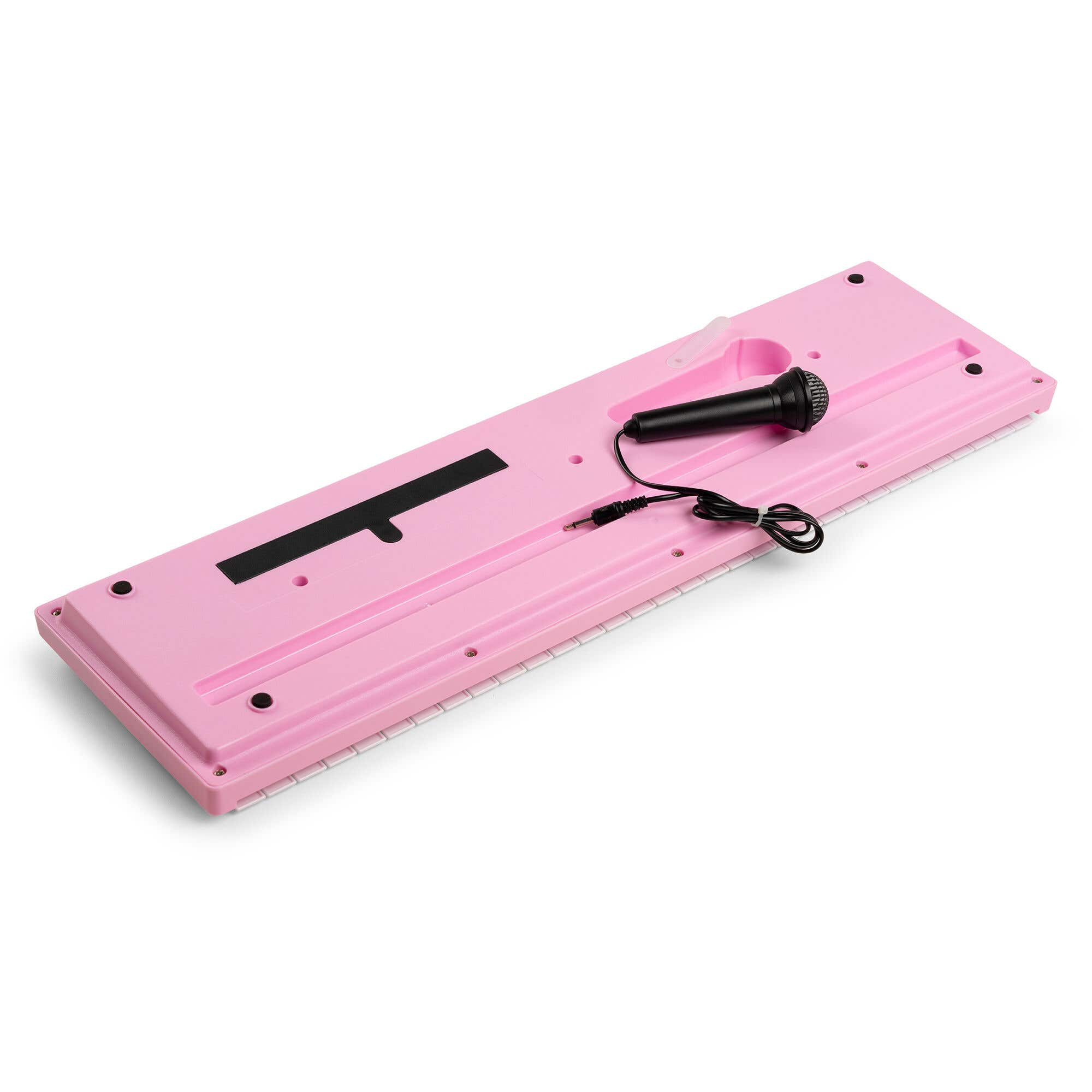 Un teclado de juguete rosa con un micrófono negro está sobre una superficie blanca. El teclado tiene una barra negra y un conector.