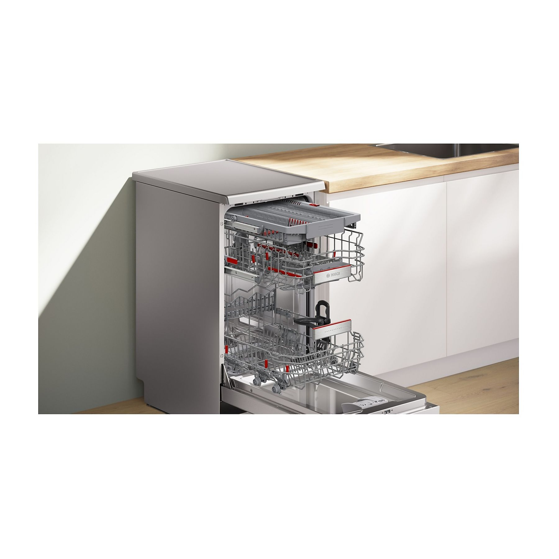 Zmywarka jest otwarta. Jest szara i ma czerwone akcenty. Za nią jest drewniany blat i białe szafki.
