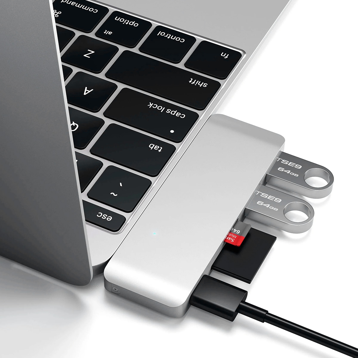 Ein silberner USB-Hub mit zwei Flash-Laufwerken, einer Speicherkarte und einem schwarzen Kabel, das mit einer Laptop-Tastatur verbunden ist.