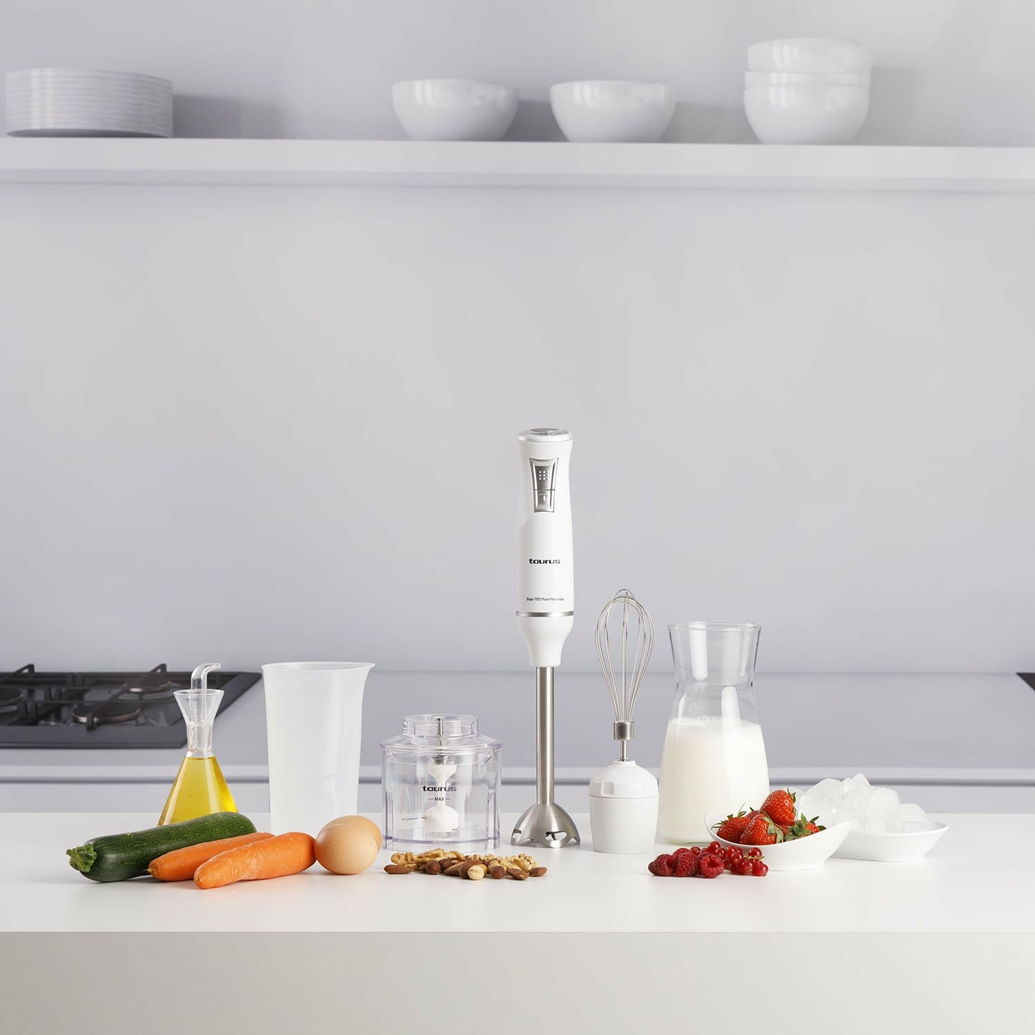 Escena de cocina con ingredientes y herramientas: batidora, calabacín, zanahorias, huevo, nueces, fresas, cubitos de hielo y leche.