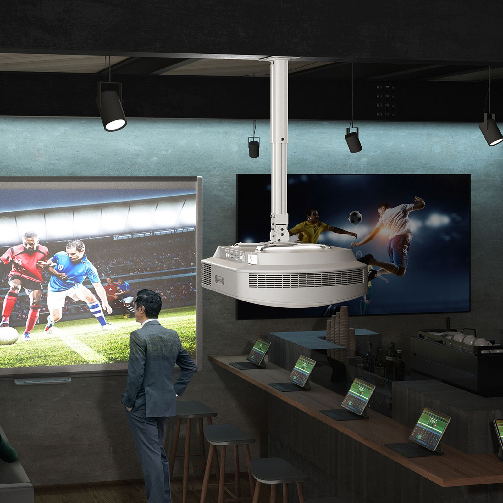 Un uomo guarda il calcio sugli schermi di un bar. Un proiettore è appeso al soffitto. Laptop sul bancone.