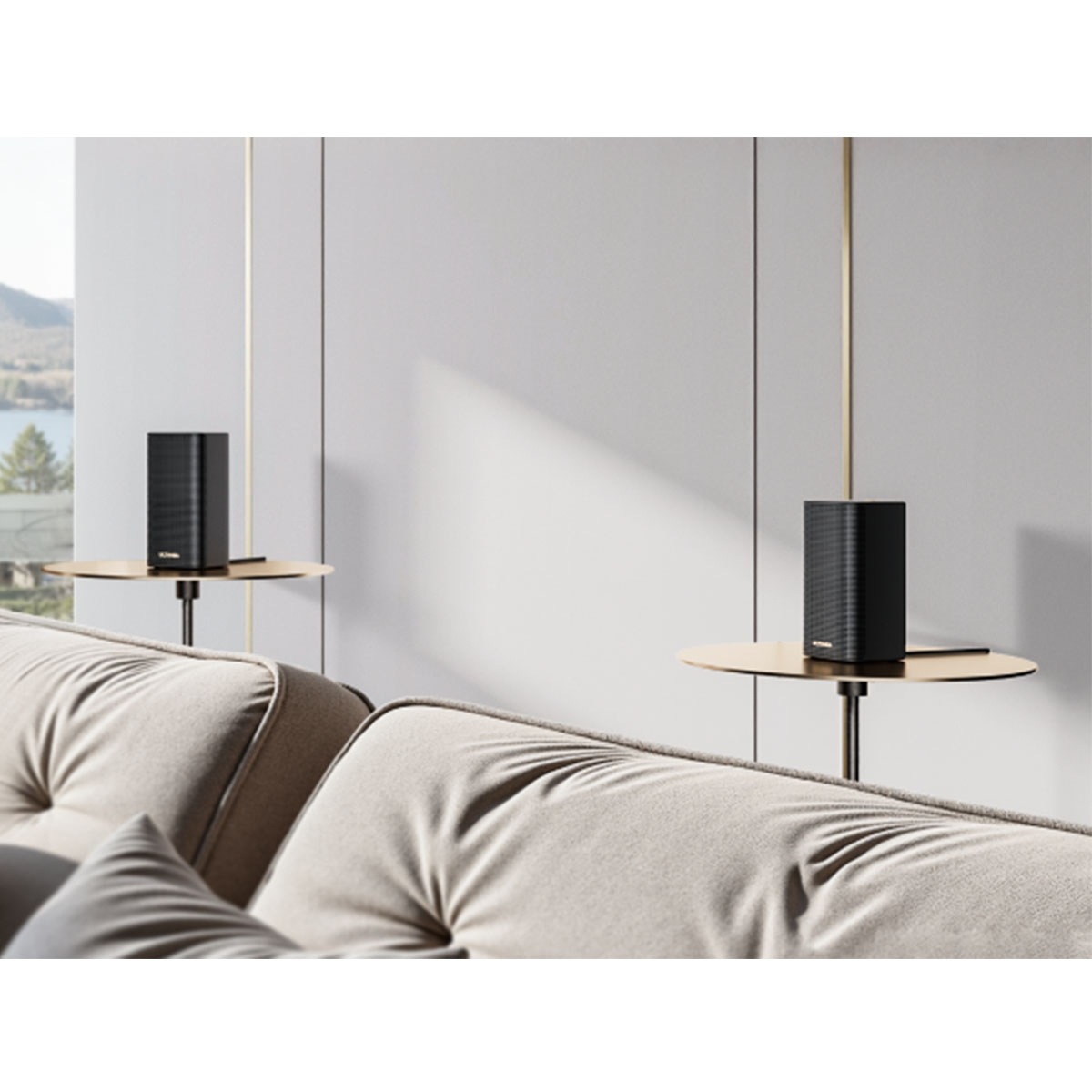 Dwa czarne głośniki na złotych stolikach obok beżowej sofy. W tle widać okno z widokiem na jezioro i białe ściany.
