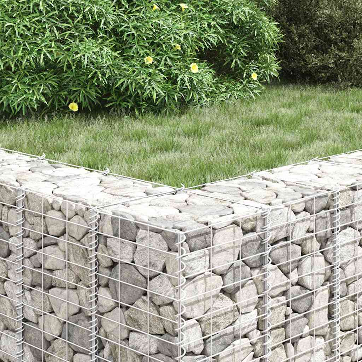 Eine Steinmauer im Garten. Grünes Gras und Blätter im Hintergrund. Gelbe Blumen säumen das Grün.