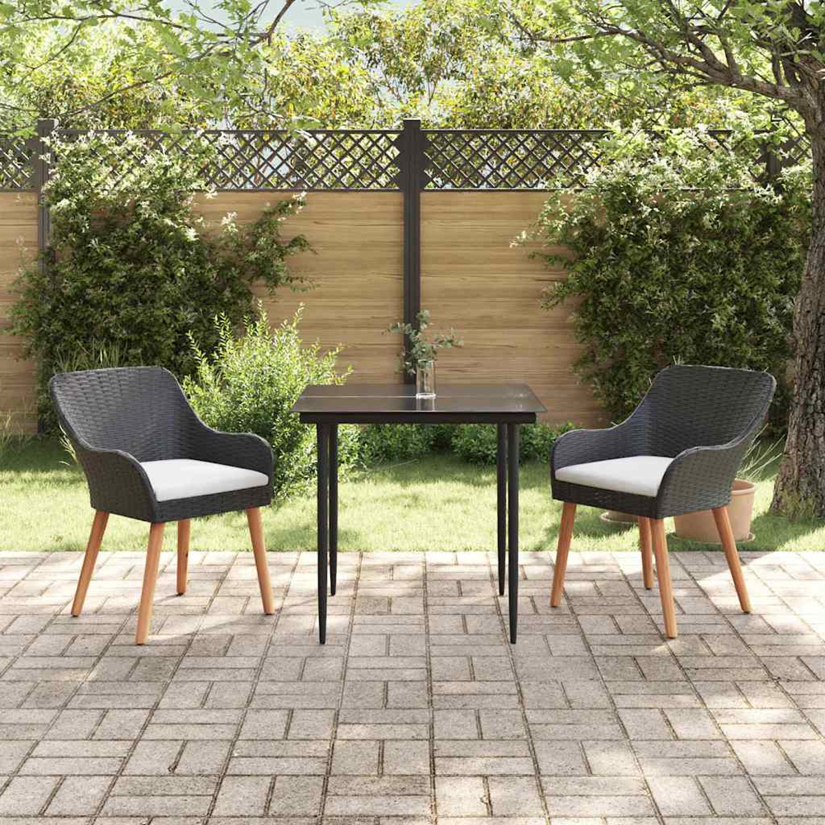 Szene auf der Terrasse mit Tisch und zwei Stühlen. Dunkle Stühle mit weißen Kissen stehen dem Tisch gegenüber. Grüne Pflanzen und Holzzaun im Hintergrund.