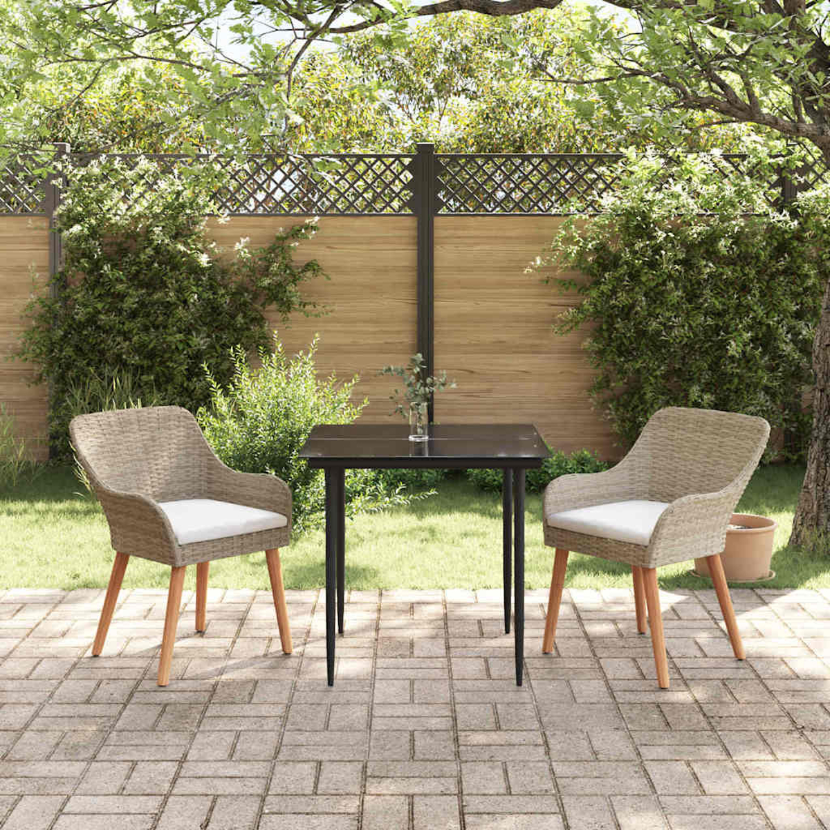 Eine Terrasse mit zwei Korbstühlen, einem schwarzen Tisch und einem Holzzaun. Pflanzen umgeben den Sitzbereich im Garten.