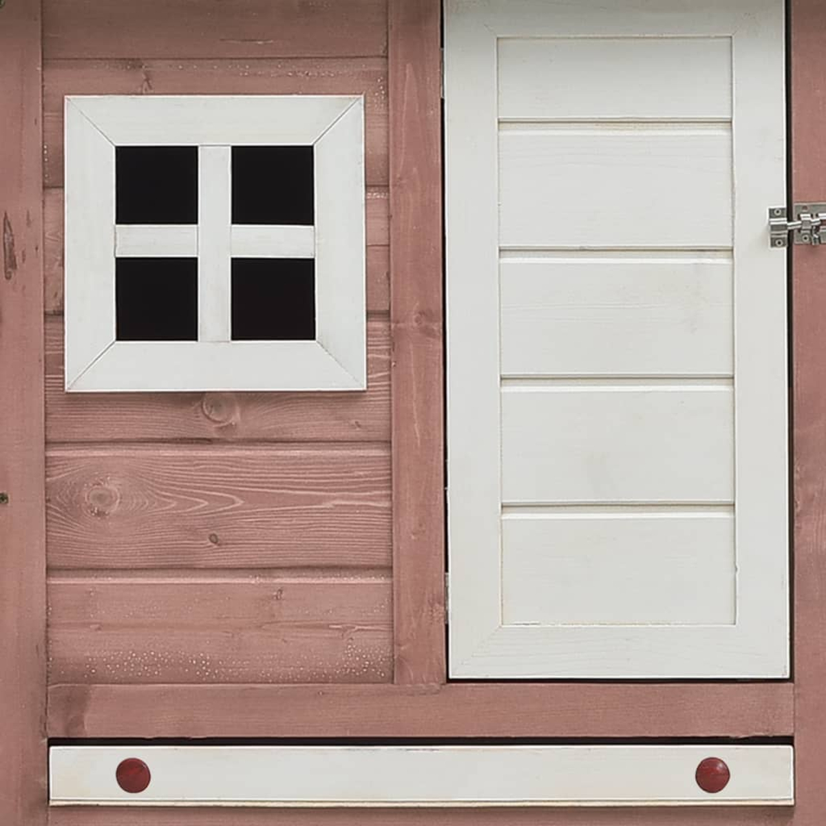 Nahaufnahme eines Holzspielhauses mit weißer Tür und Fenster. Das Fenster hat ein Kreuzdesign, und die Tür ist geschlossen.