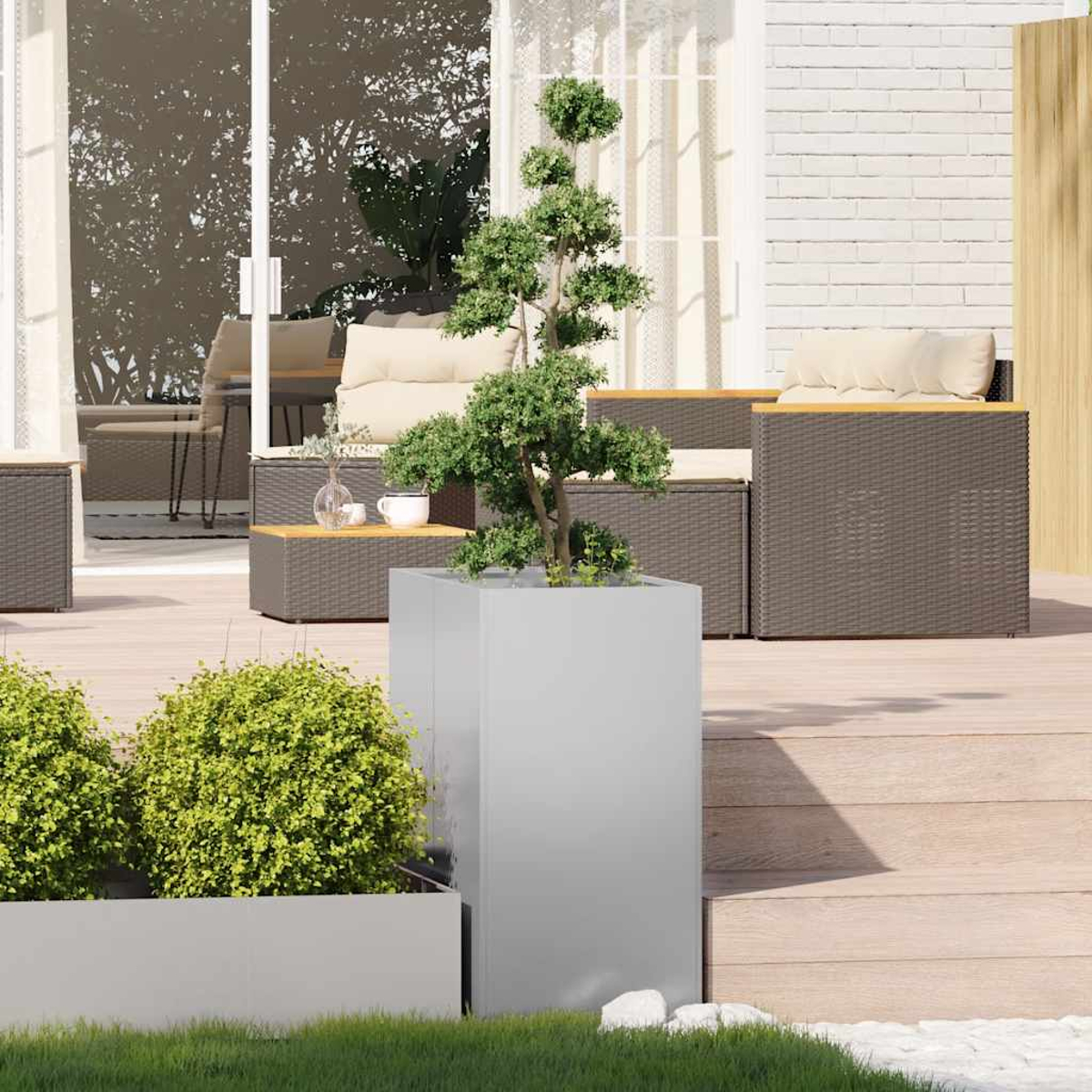 Scena all'aperto con un bonsai in una fioriera argentata, mobili in vimini e cespugli verdi. Muro di mattoni bianchi e patio.