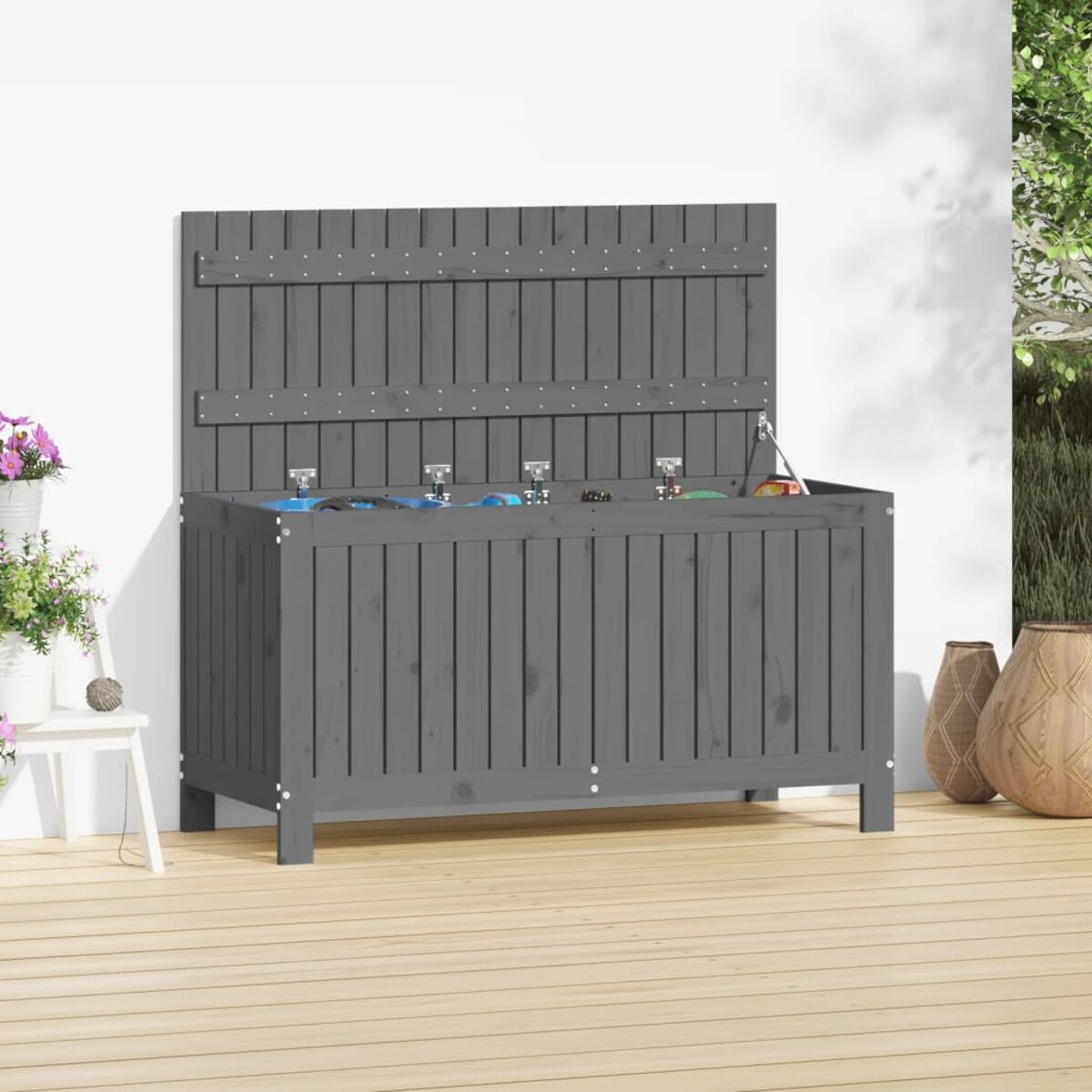 Un contenitore di legno grigio con coperchio aperto, su un ponte di legno. Fiori in vasi bianchi e vasi decorativi nelle vicinanze.