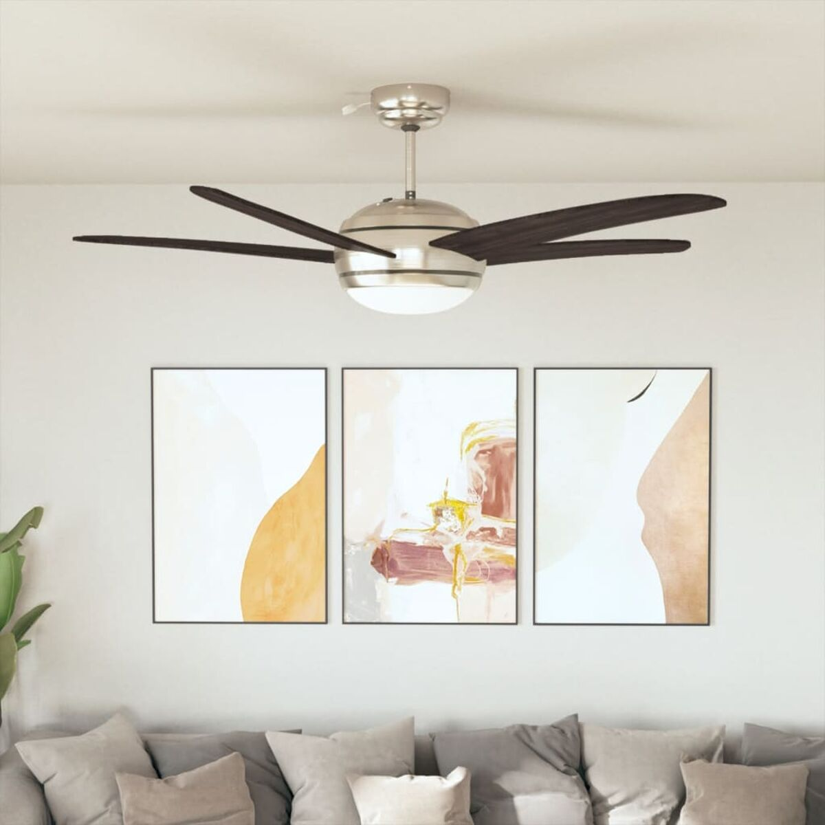 Un ventilatore a soffitto, arte astratta e un divano con cuscini sono nella stanza. Il ventilatore ha pale marroni scure. L'arte è in cornici nere.