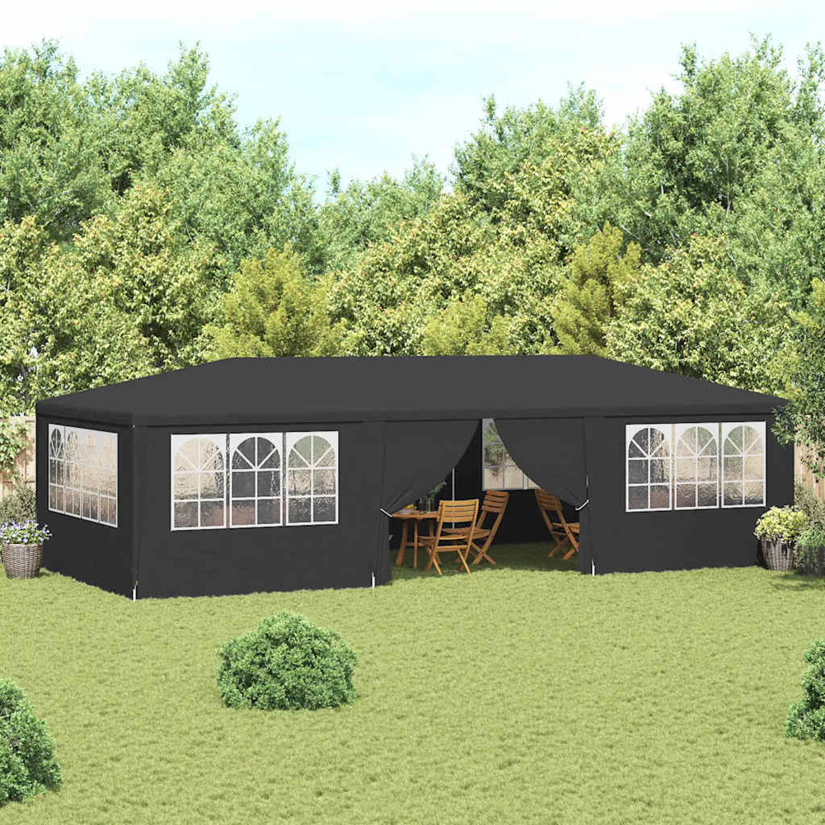 Una tenda nera con finestre incorniciate di bianco è su un prato. All'interno, un tavolo e sedie. Gli alberi sono sullo sfondo.