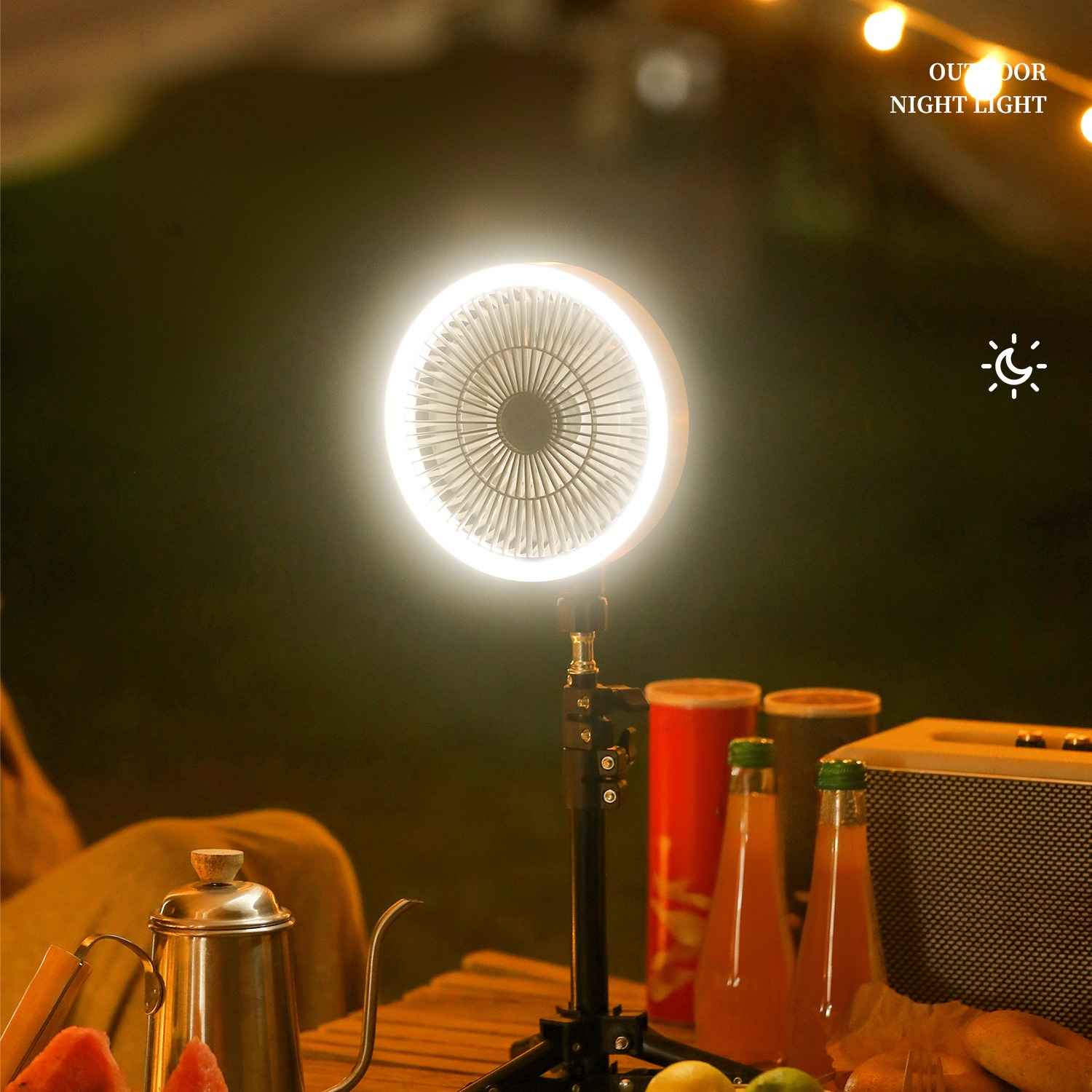 Eine leuchtende Campinglampe beleuchtet einen Tisch mit Getränken und Essen. Eine Metallkanne und Lautsprecher sind ebenfalls zu sehen.