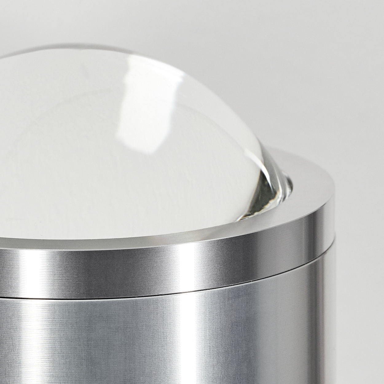 Nahaufnahme eines metallischen Zylinders mit gewölbtem Glasdeckel. Das Metall hat ein gebürstetes Finish, das Glas ist klar.