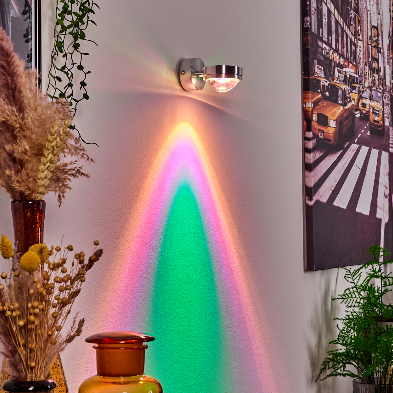 Eine Wandlampe projiziert einen bunten Bogen an die Wand. Trockenblumen und ein NYC-Taxi-Druck schmücken den Raum.