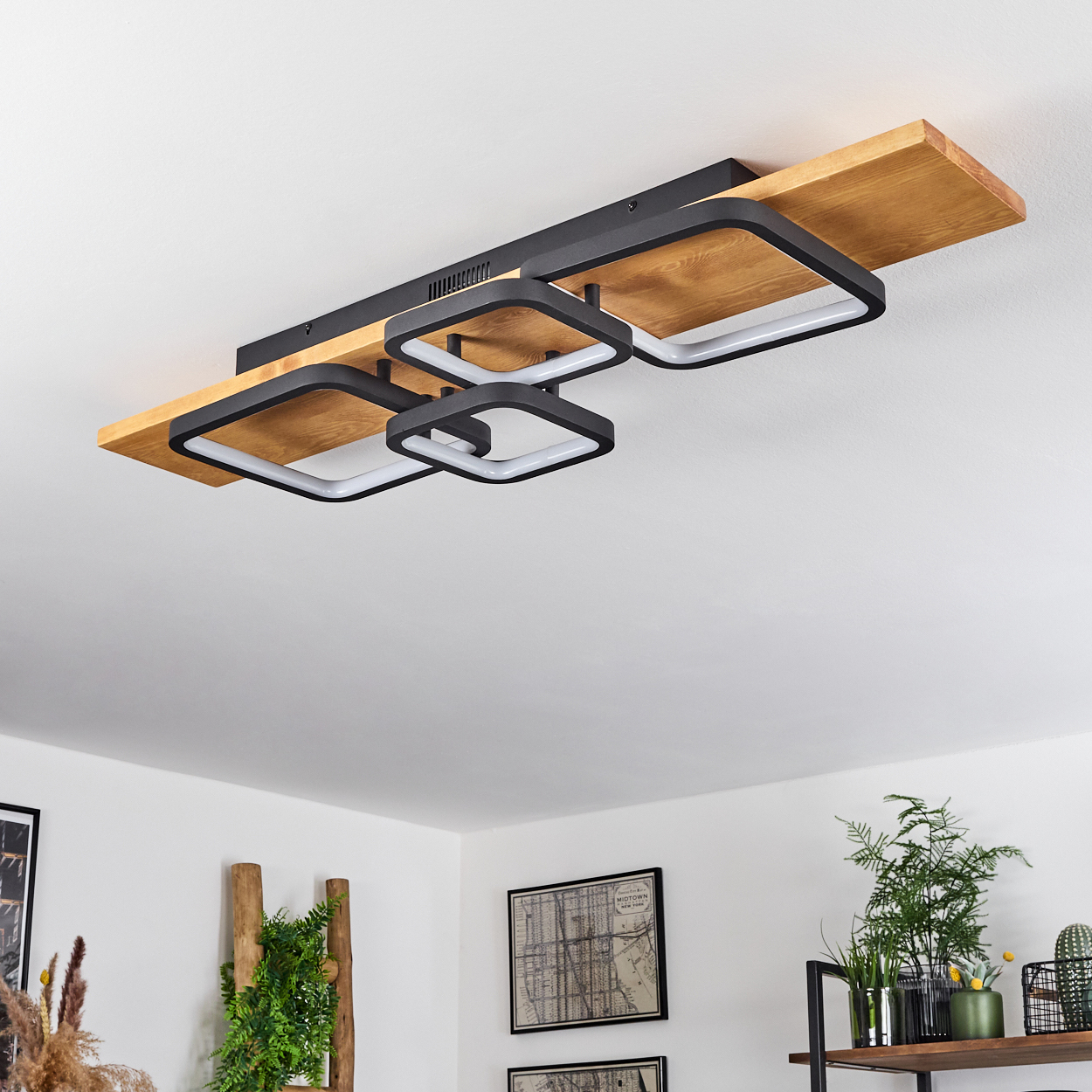 Eine moderne Deckenleuchte mit quadratischen Lampen auf Holzbalken. Der Hintergrund zeigt eine weiße Decke und Wände mit Dekorationsartikeln.