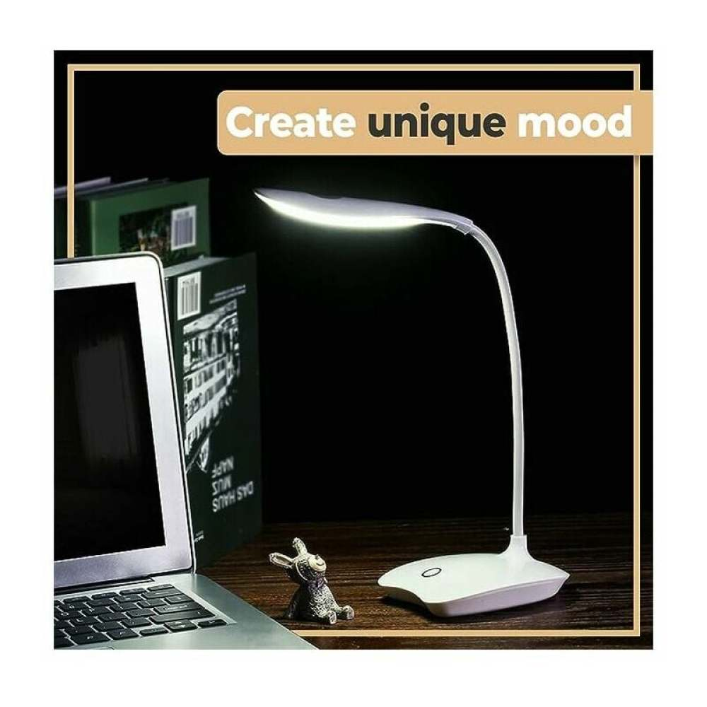 Eine weiße Schreibtischlampe leuchtet auf einer Holzoberfläche. Ein Laptop, Bücher und eine kleine Hasenfigur sind ebenfalls vorhanden.