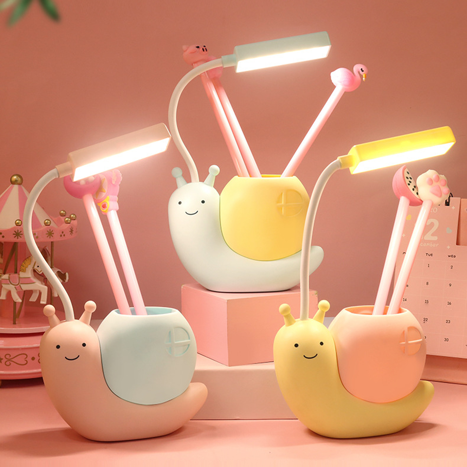 Drei schneckenförmige Schreibtischlampen mit Stiften. Rosa Hintergrund. Einer hat einen Flamingo, einer ein Schwein, einer eine Pfote.
