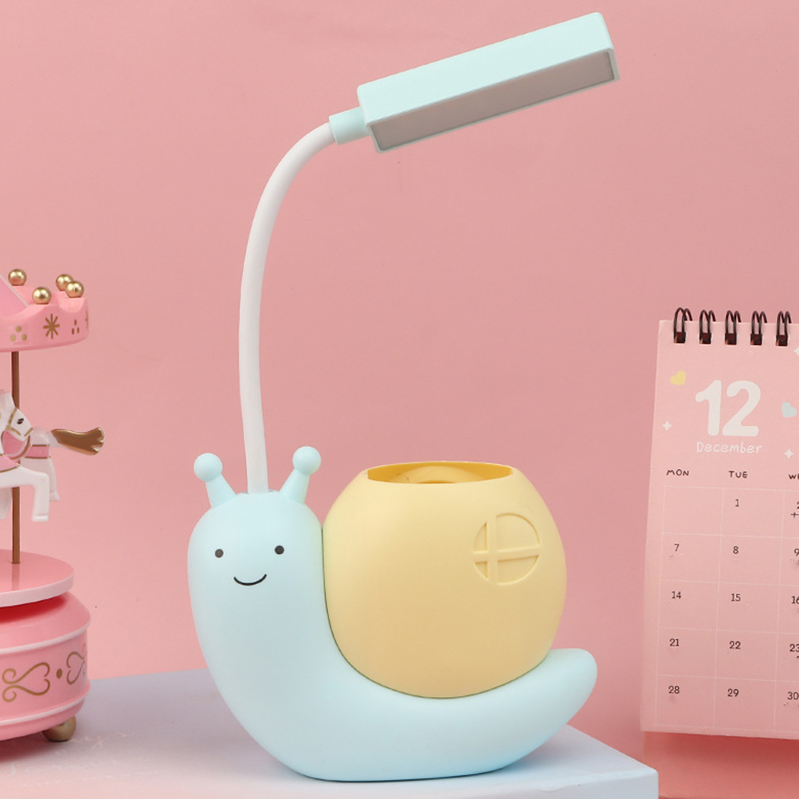 Eine schneckenförmige Lampe mit Stifthalter. Rosa Hintergrund mit Karussell und Kalender.