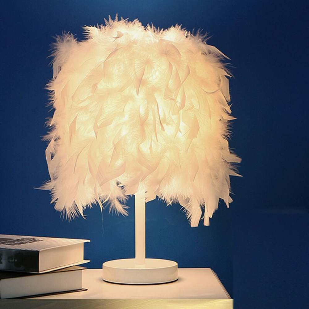 Eine weiße Federlampe steht auf einem Tisch mit Büchern. Der Hintergrund ist eine dunkelblaue Wand. Die Lampe ist an.