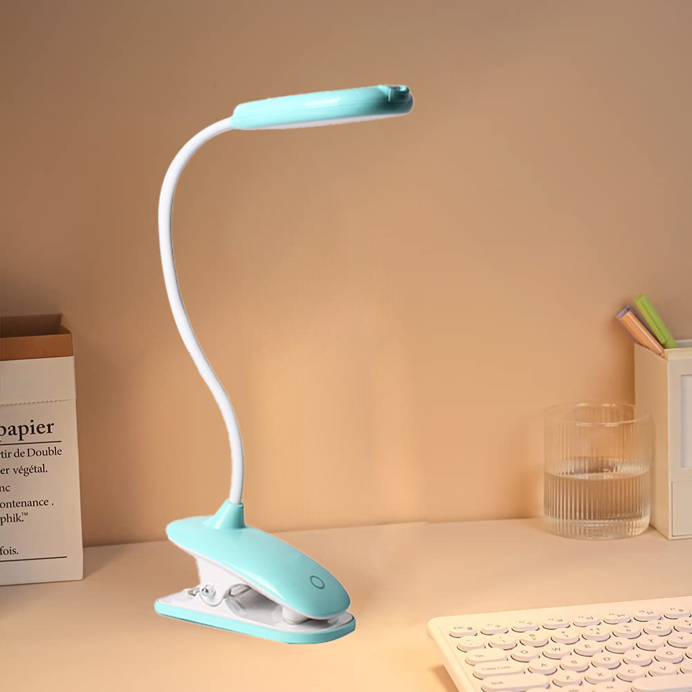 Eine Schreibtischlampe mit blaugrünem Kopf und Sockel, weißem flexiblem Arm und Clip. Sie steht auf einem Schreibtisch mit Tastatur und Wasserglas.