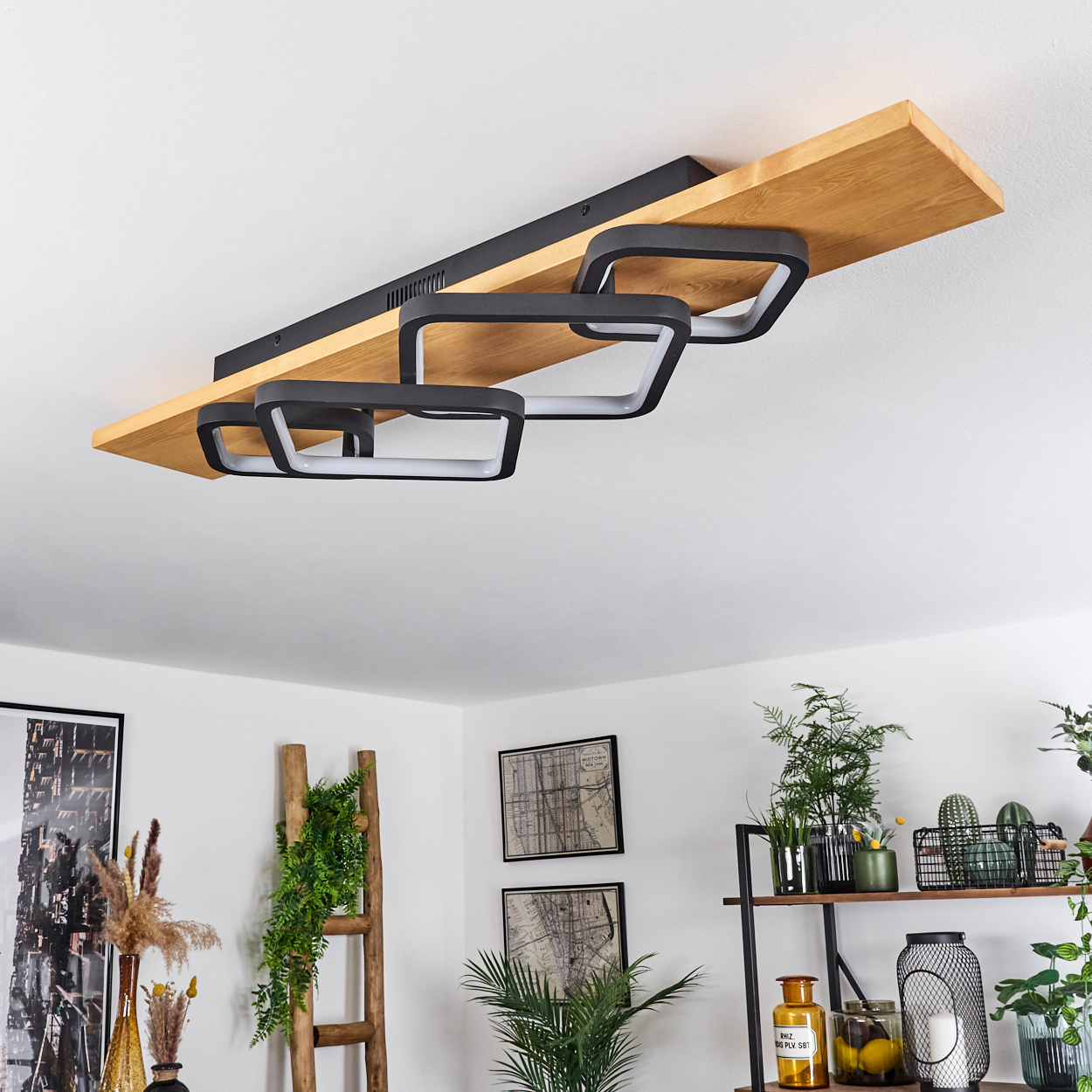 Deckenleuchte mit schwarzen quadratischen Rahmen und Holzbrett. Zimmer mit Pflanzen, Leiter und gerahmten Karten.