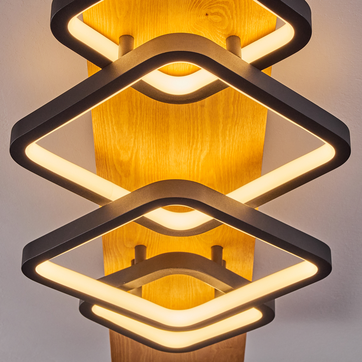 Eine moderne Deckenleuchte mit Holzrücken. Sie hat vier rautenförmige Lichtpaneele mit warmweißem Licht.