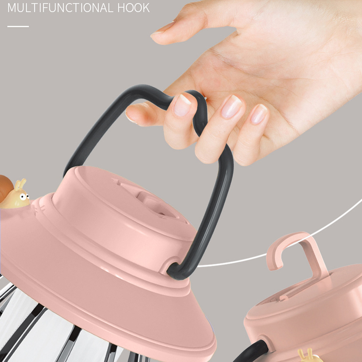 Eine Hand hält eine rosa Lampe mit schwarzem Griff. Eine kleinere Lampe mit Haken ist sichtbar. Ein kleines gelbes Wesen ist zu sehen.