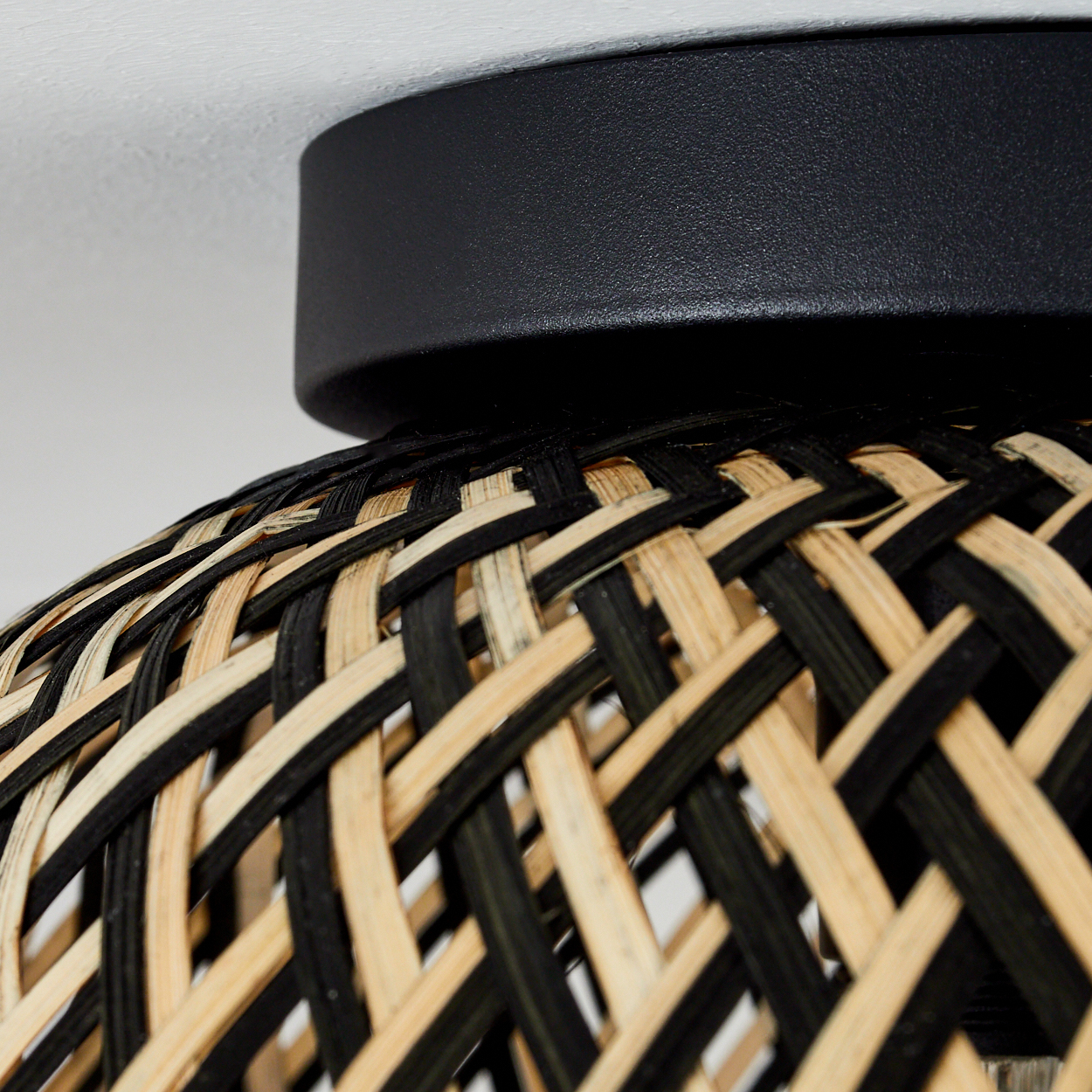 Nahaufnahme einer Lampe. Sie hat einen schwarzen Metallsockel und einen gewebten Lampenschirm in Schwarz- und Naturtönen.