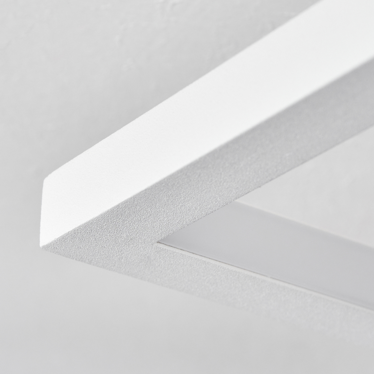 Nahaufnahme eines weißen, rechteckigen Rahmens mit strukturierter Oberfläche vor weißem Hintergrund. Der Innenbereich ist mit weißem Licht beleuchtet.