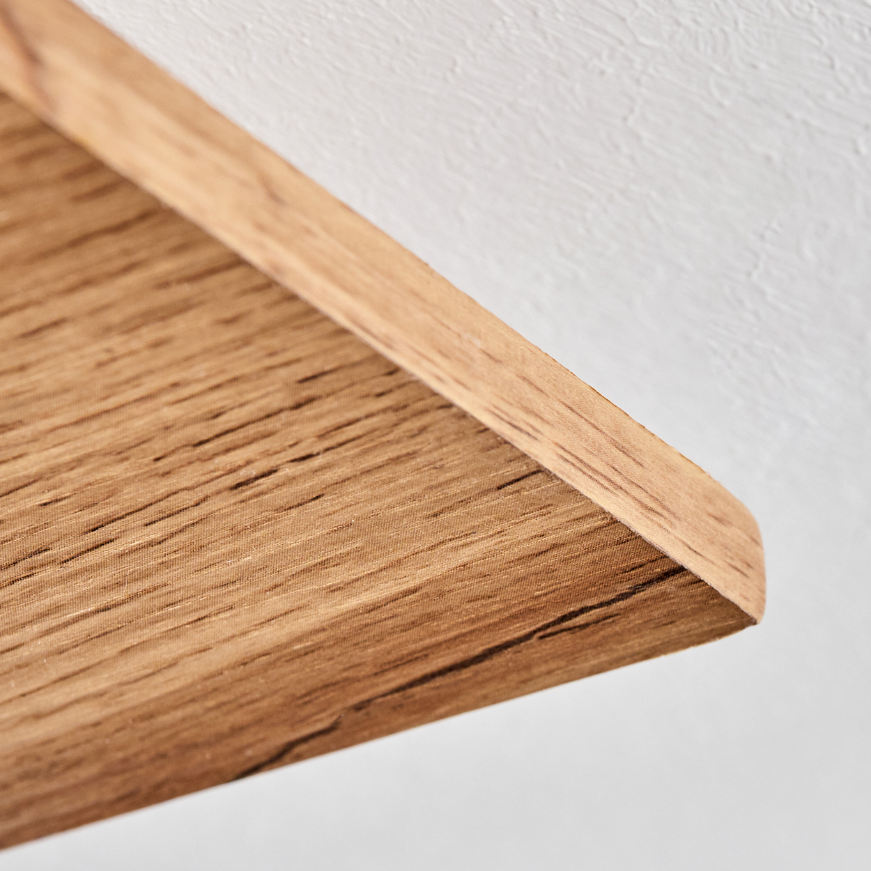 Nahaufnahme eines Holzregals mit abgerundeter Kante. Das Holz hat eine natürliche Maserung. Der Hintergrund ist eine weiße, strukturierte Wand.