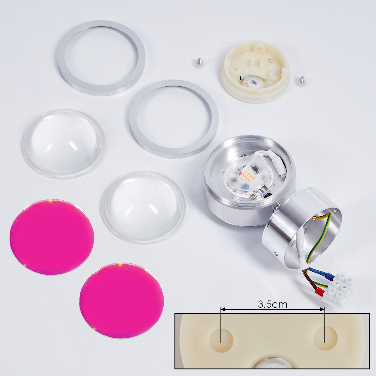 Zerlegte LED-Leuchtkomponenten auf weißer Oberfläche. Enthält Metallringe, Linsen, pinkfarbene Kreise und eine Leuchte mit Drähten. Eine 3,5 cm Messung wird gezeigt.