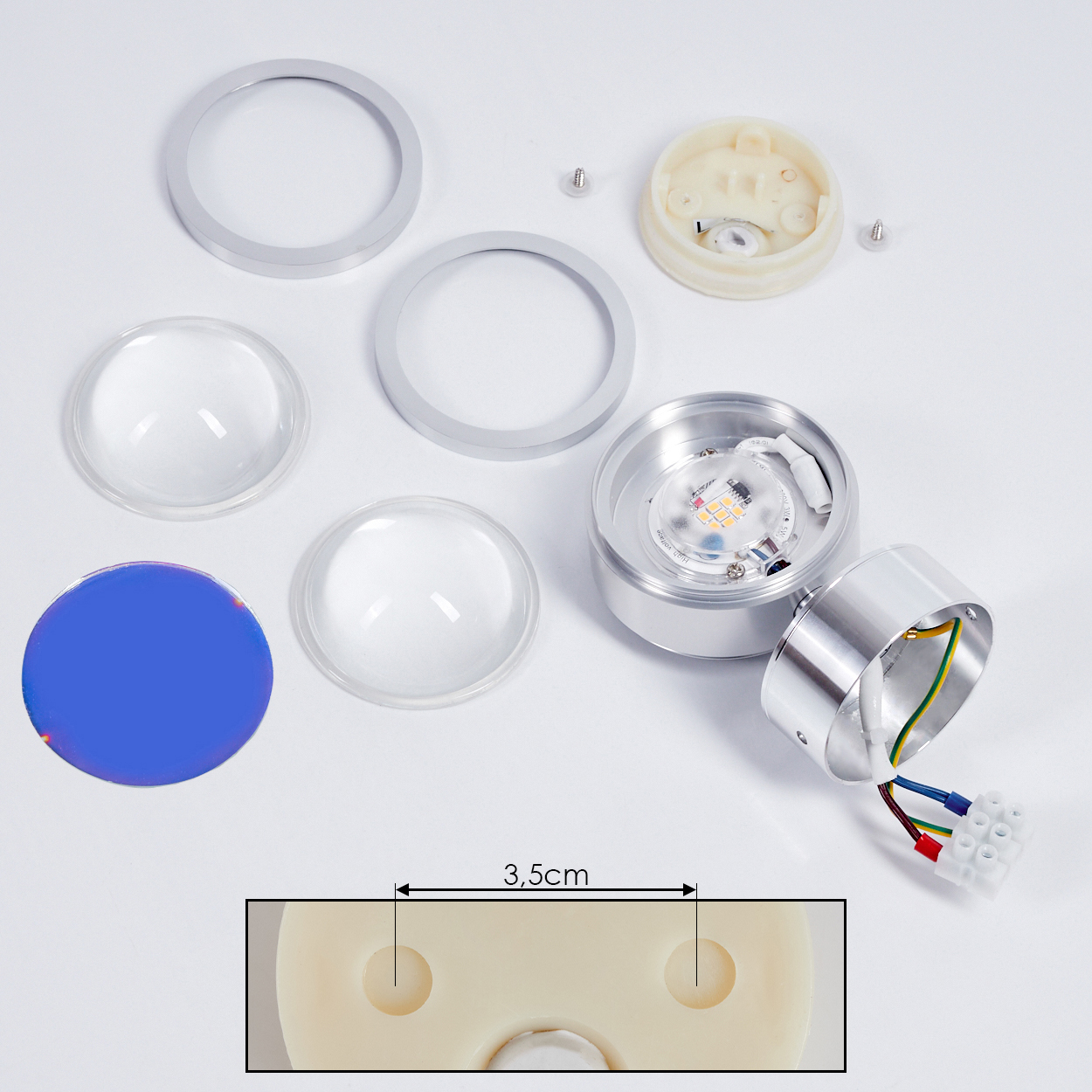 Zerlegte LED-Lichtkomponenten auf weißer Oberfläche. Enthält Metallringe, Linsen, LED, Schrauben und eine blaue Scheibe.
