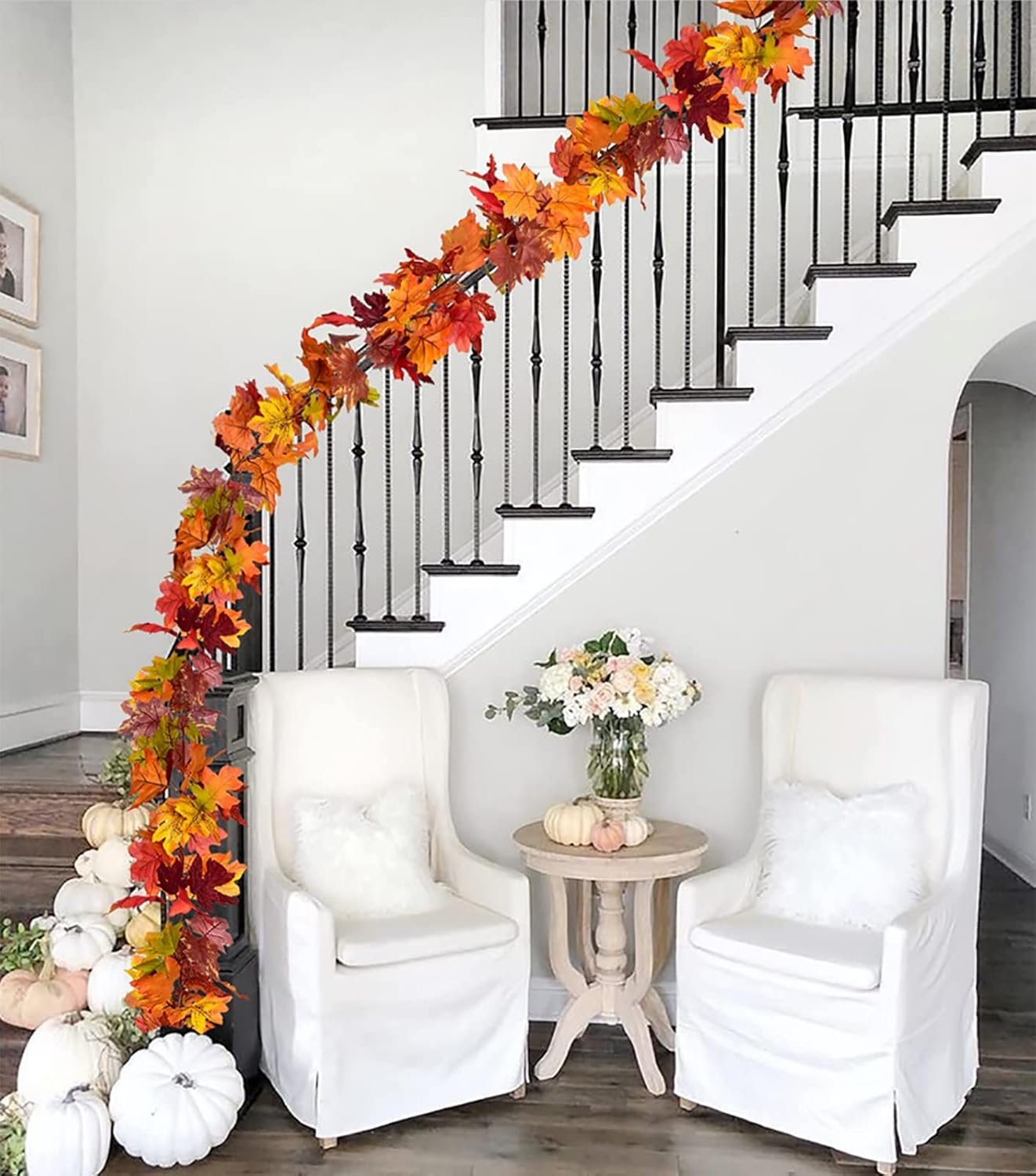 Eine Treppe ist mit Herbstblättern geschmückt. Vorne stehen zwei weiße Stühle und ein kleiner Tisch mit Blumen und Kürbissen.