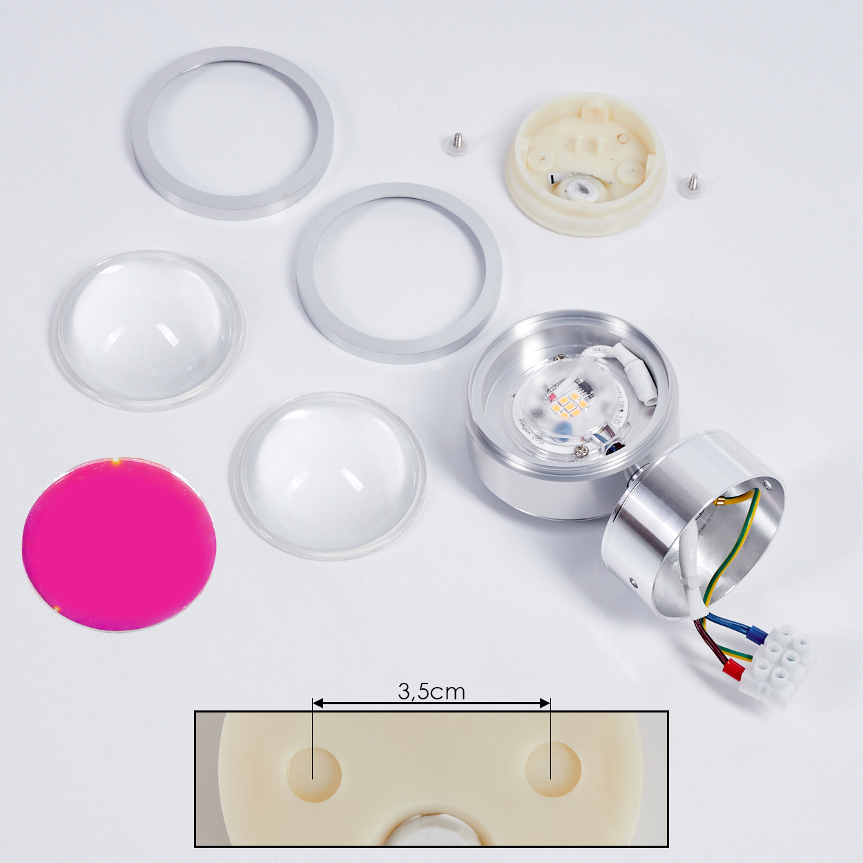 Zerlegte LED-Leuchtenkomponenten auf Weiß. Enthält Linsen, Ringe, eine rosa Scheibe, Metallgehäuse mit Drähten und eine kleine Basis.