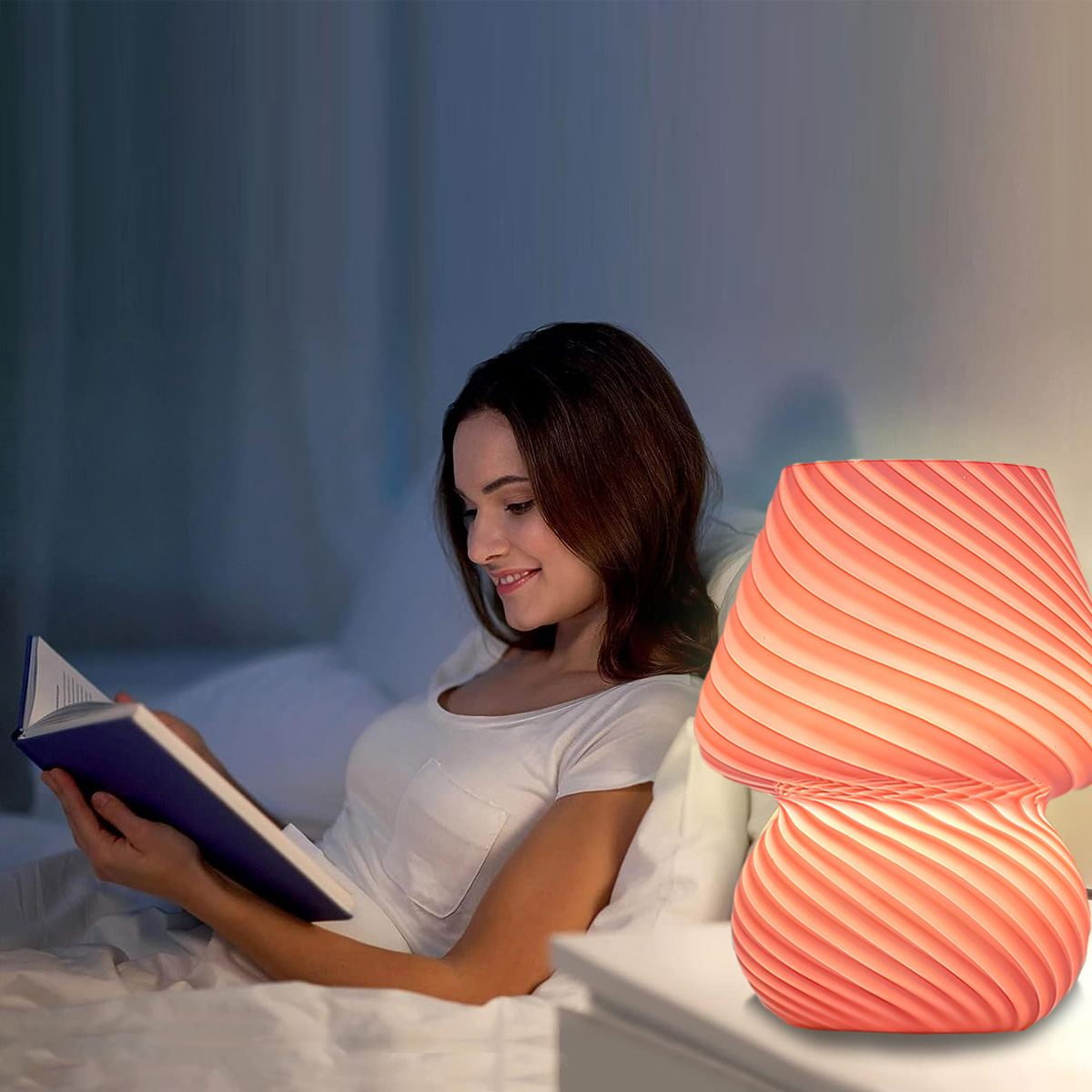 Eine Frau liest im Bett, beleuchtet von einer pilzförmigen Lampe. Die pfirsichfarbene Lampe steht auf einem Nachttisch. Sie lächelt das Buch an.