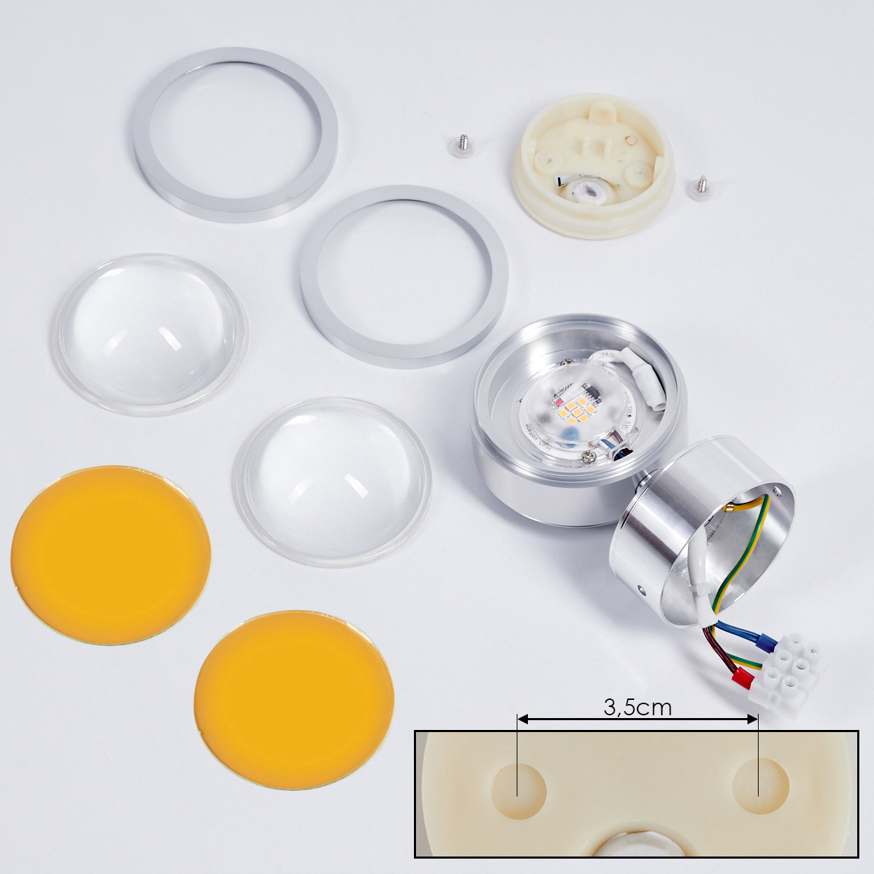 Zerlegte LED-Leuchtenkomponenten auf weißer Oberfläche. Enthält Metallteile, Linsen, gelbe und klare Scheiben und einen Kabelanschluss.