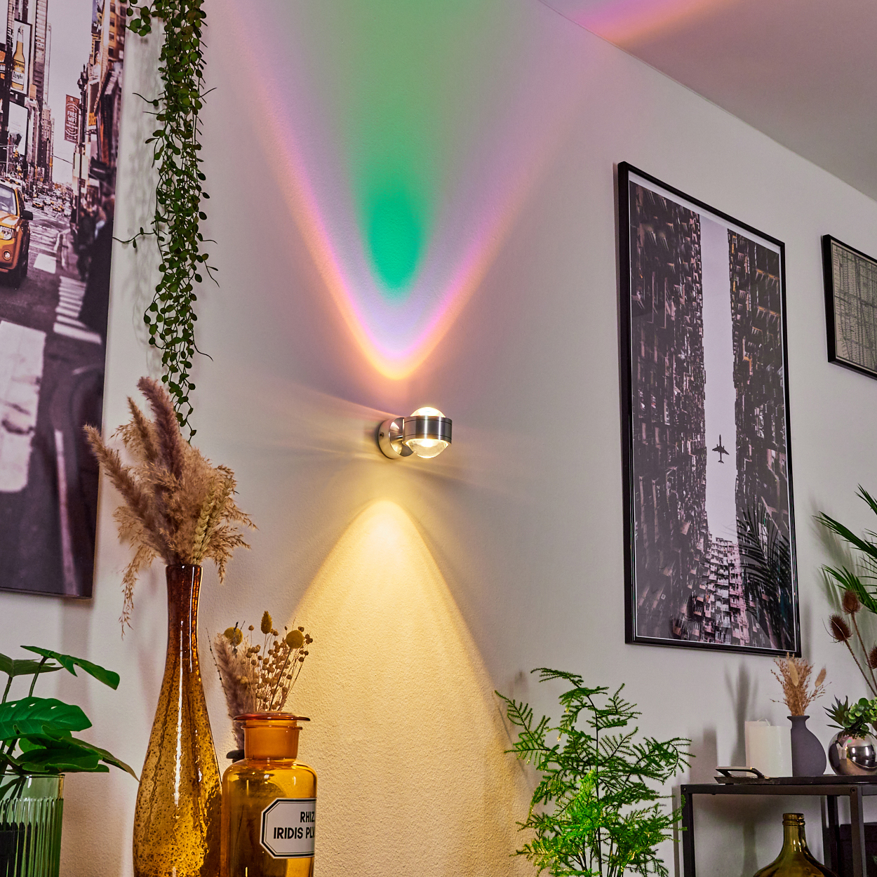 Eine Wandlampe projiziert farbenfrohe Lichtmuster. Kunstwerke und Pflanzen schmücken den Raum. Im Hintergrund ist ein gelbes Taxi zu sehen.
