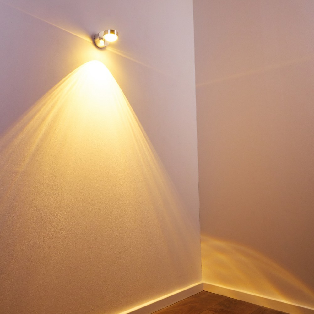 Ein Scheinwerfer an der Decke beleuchtet eine Ecke eines Raumes und wirft einen hellen Strahl auf die Wand. Die Wand ist weiß und der Boden ist aus Holz.