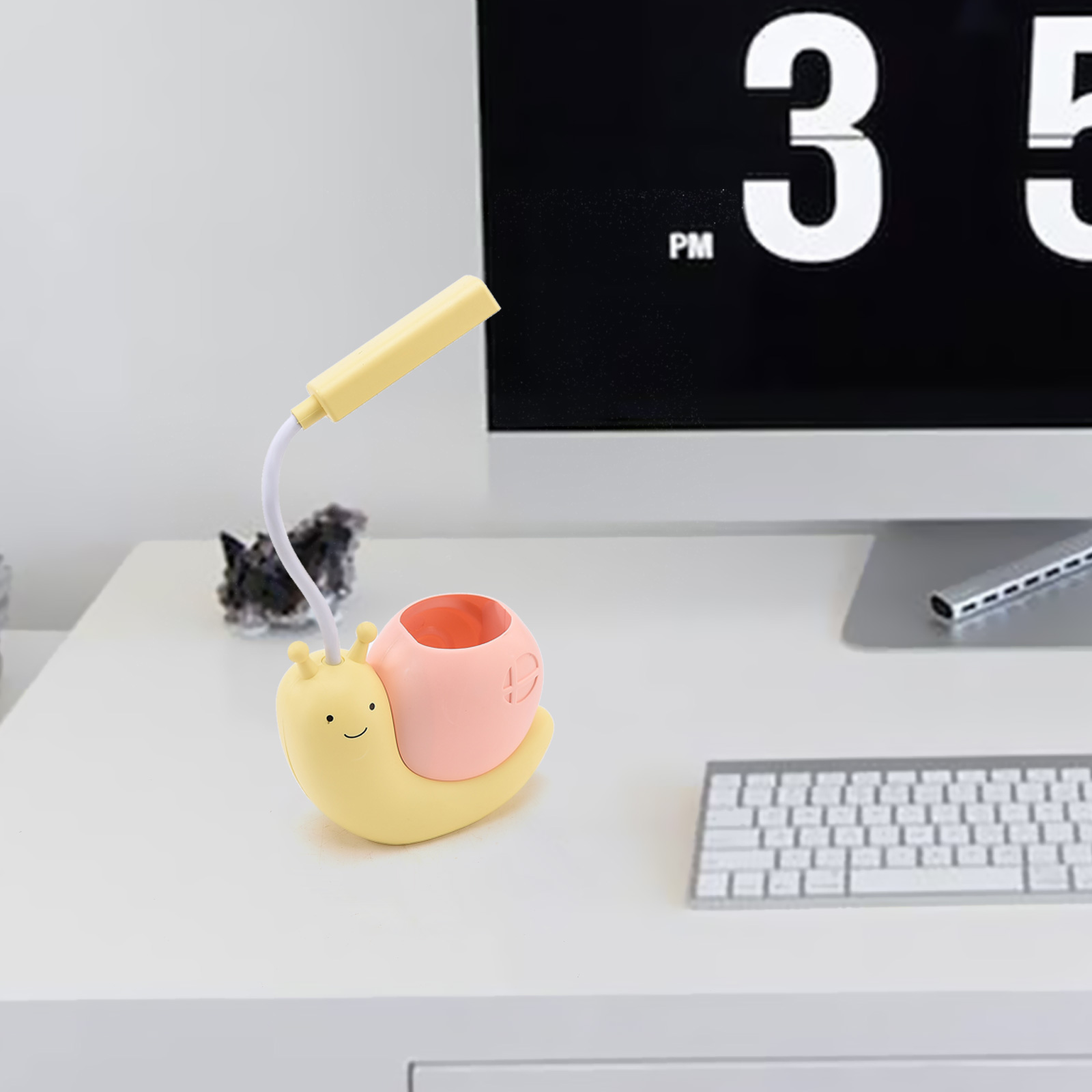 Ein Schreibtisch mit einer schneckenförmigen Schreibtischlampe. Die Lampe ist gelb und rosa. Im Hintergrund befinden sich ein Computer und eine Tastatur.
