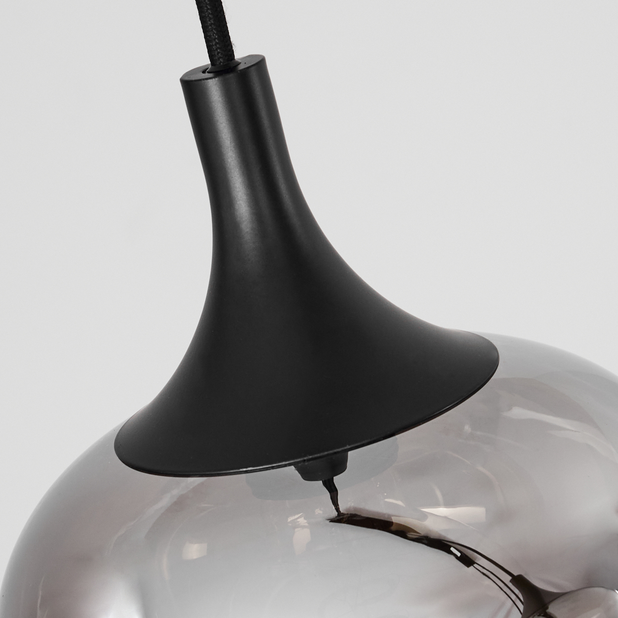 Eine moderne Pendelleuchte mit schwarzem Oberteil und grauem, reflektierendem Glasschirm, vor weißem Hintergrund.