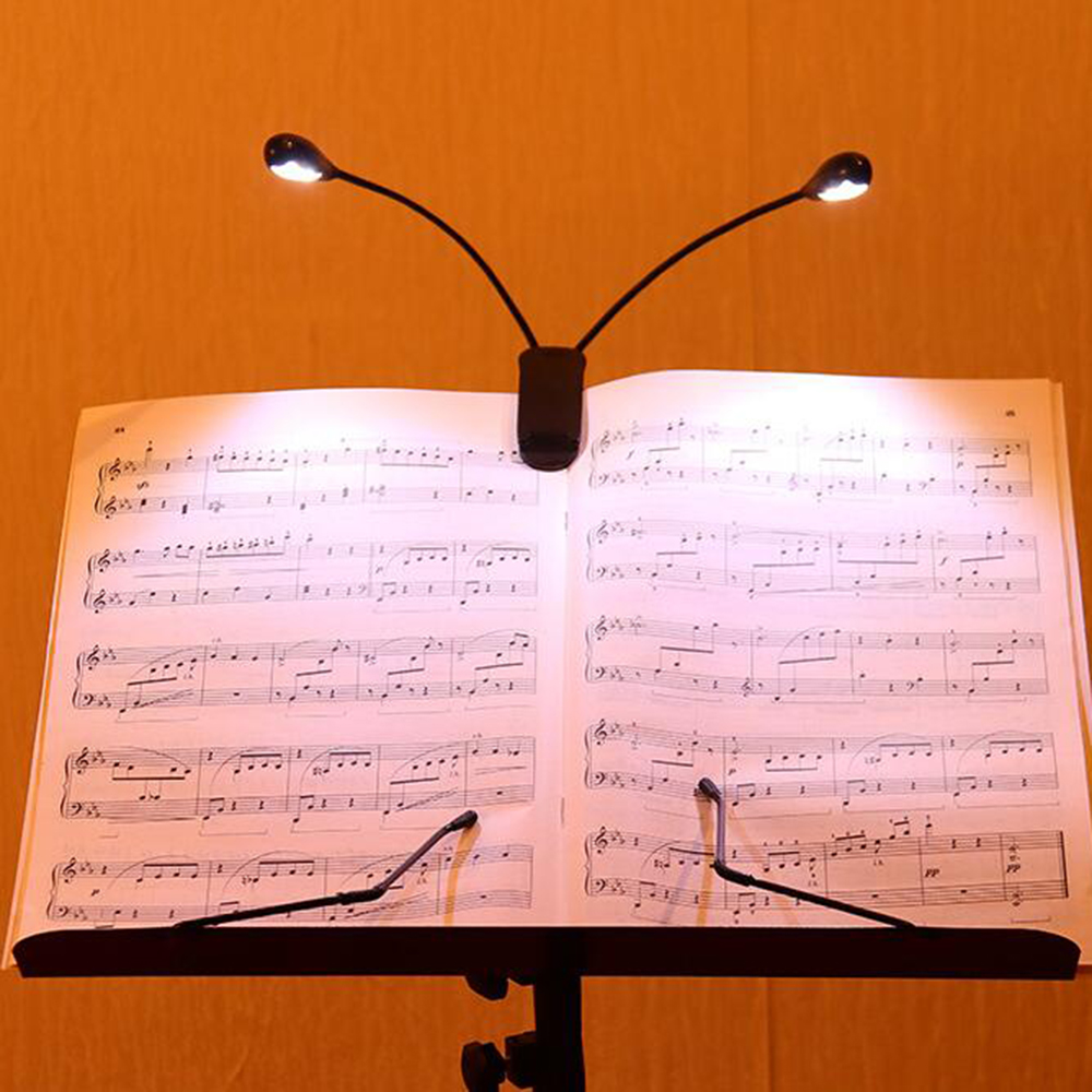 Noten auf einem Ständer, beleuchtet von zwei kleinen Lampen. Schwarzer Ständer und Lampen, weißes Papier mit Noten, vor gelbem Hintergrund.